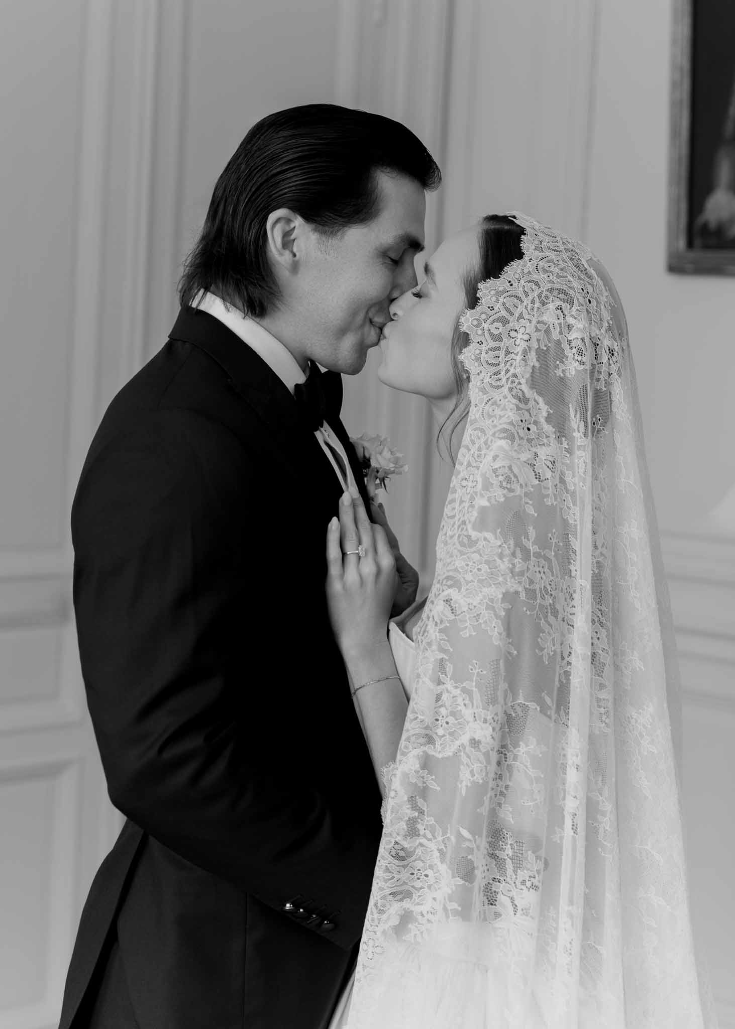 Black and white close-up of bride in Mantilla lace veil kissing groom in chateau interior