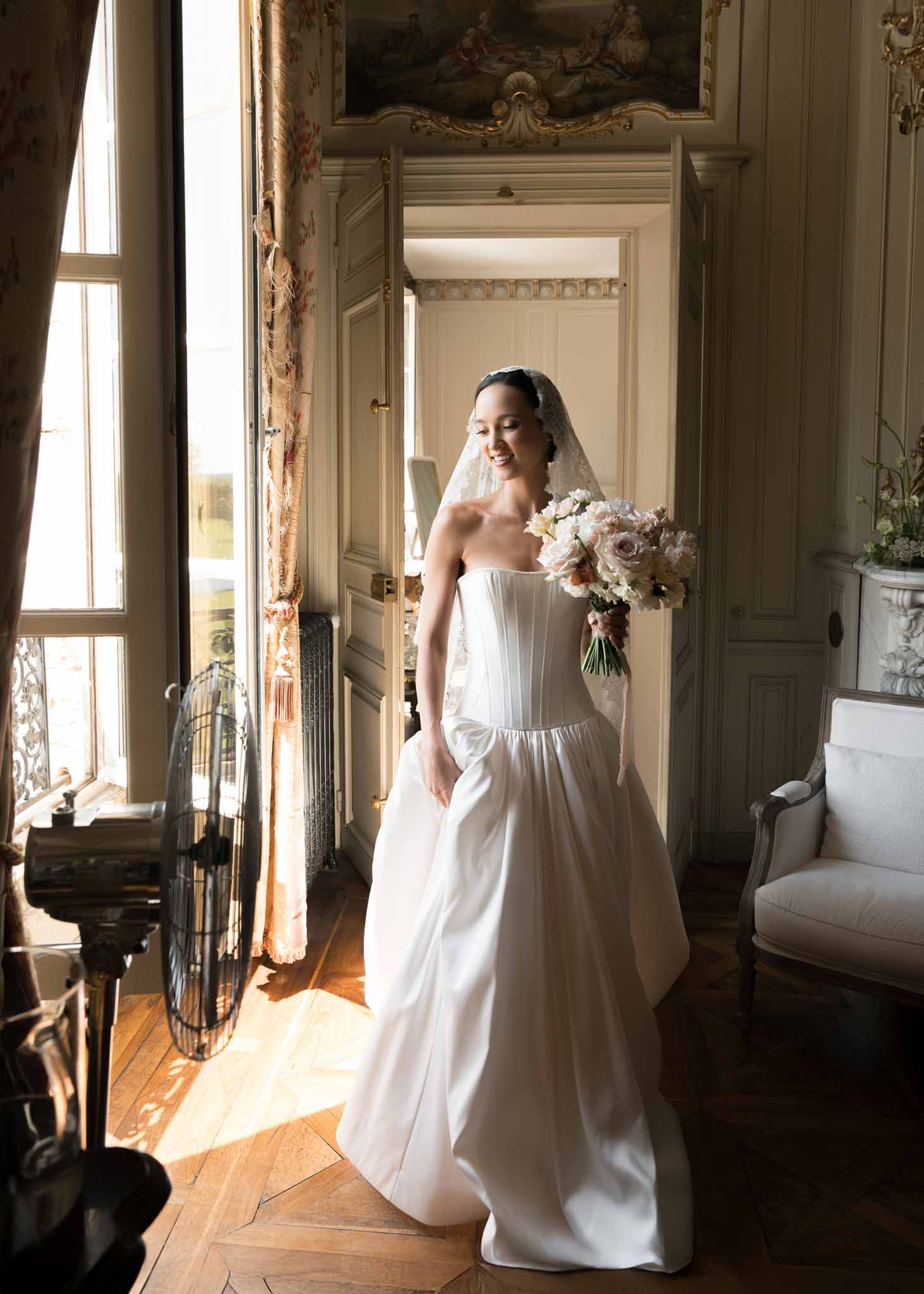Bride in strapless ballgown with lace veil standing in gilded rococo chateau doorway