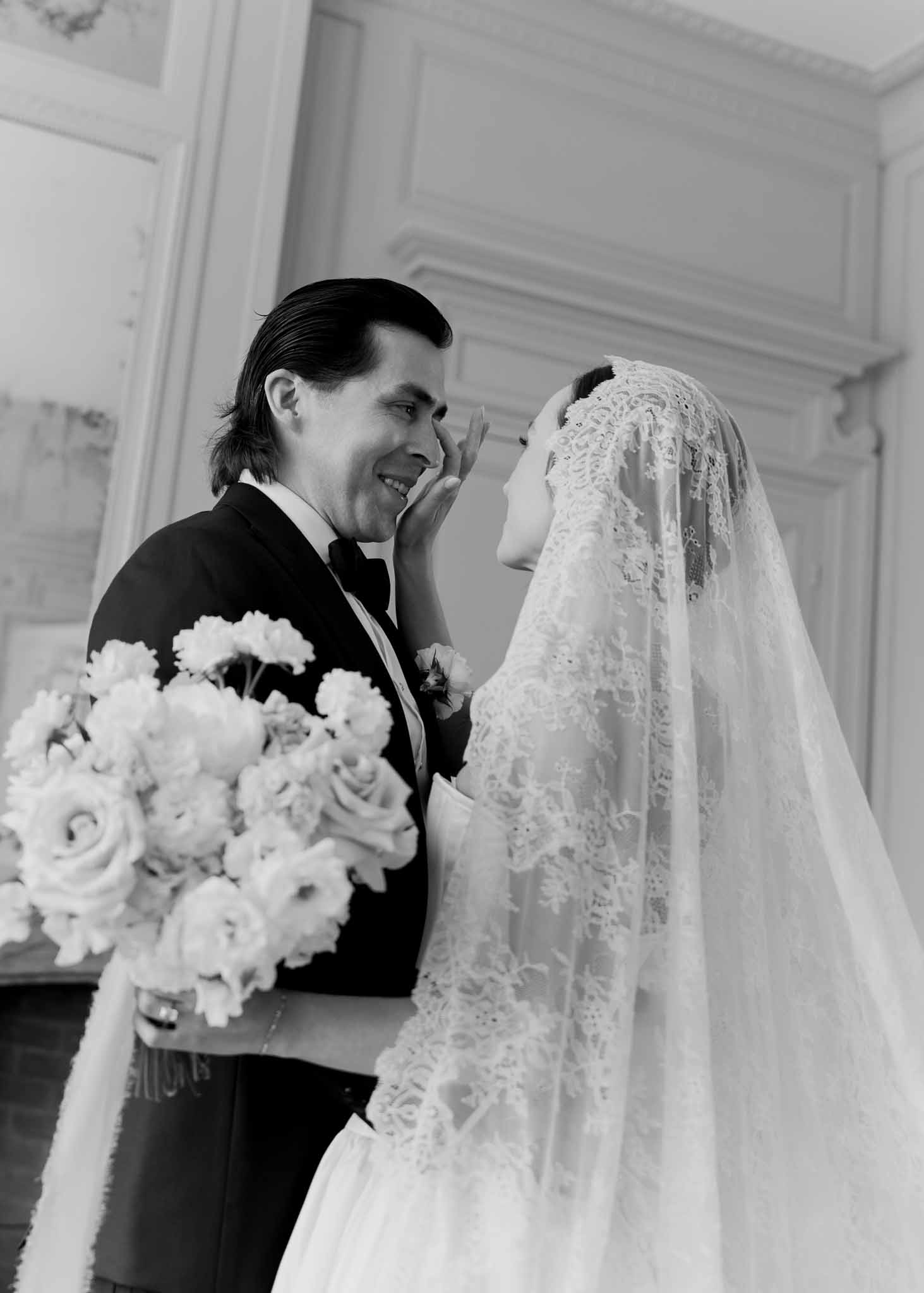 Black and white close-up of bride touching groom's cheek through lace mantilla veil