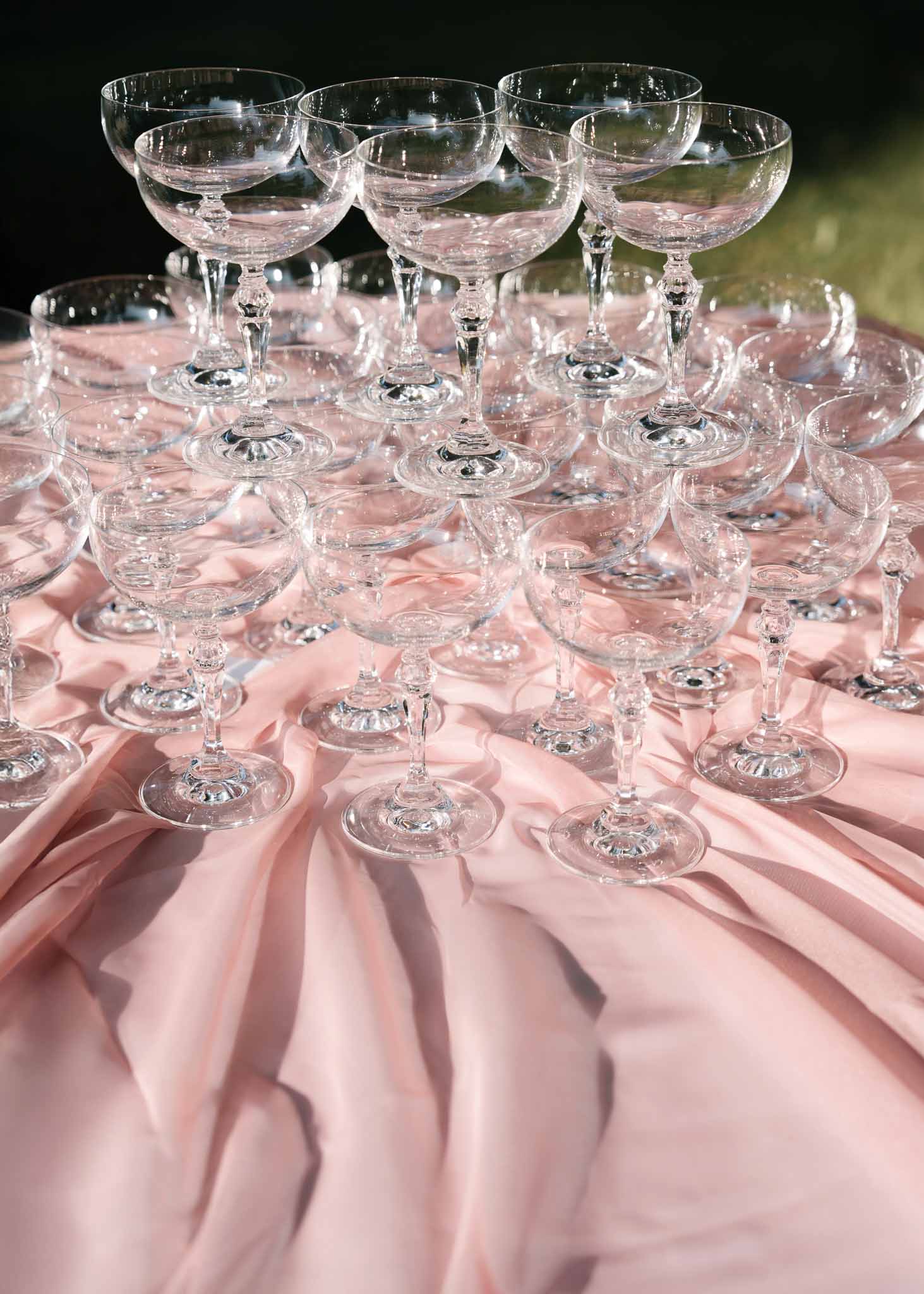 Vintage crystal champagne coupe glasses arranged on a round table with blush pink satin tablecloth