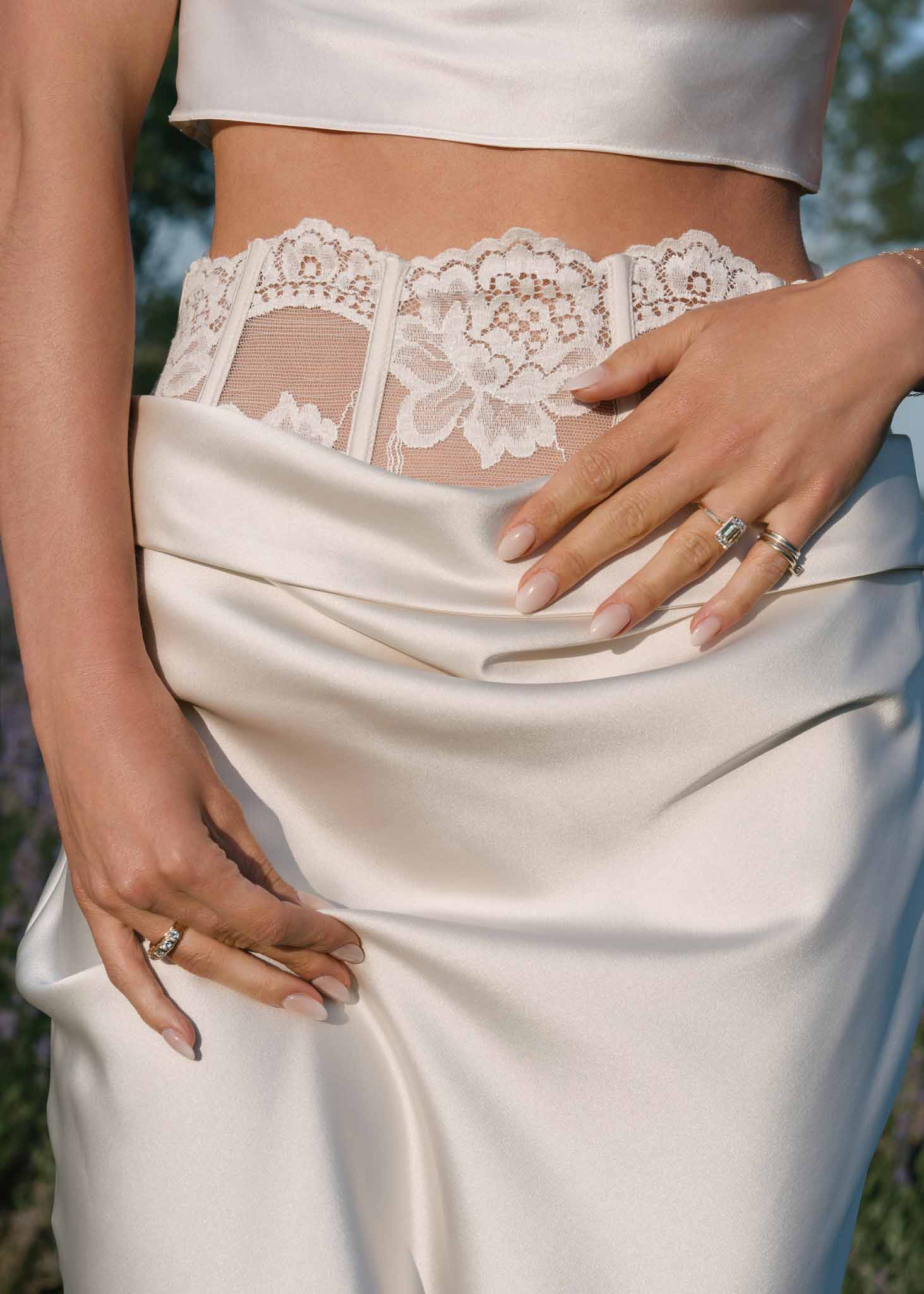 Close-up of two-piece bridal outfit with satin crop top, draped skirt, and sheer lace corset waist belt