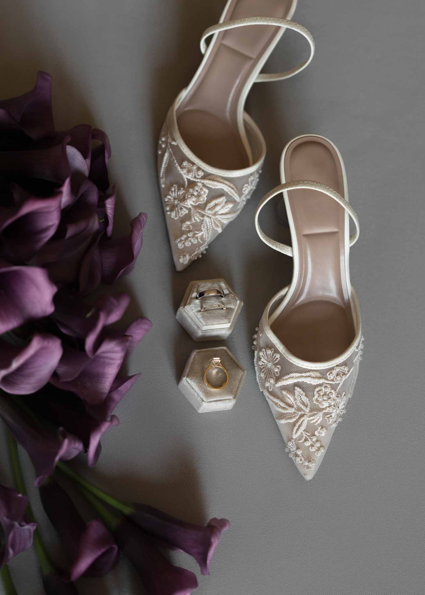 Ivory embroidered slingback bridal heels with velvet ring boxes and plum calla lilies on grey surface