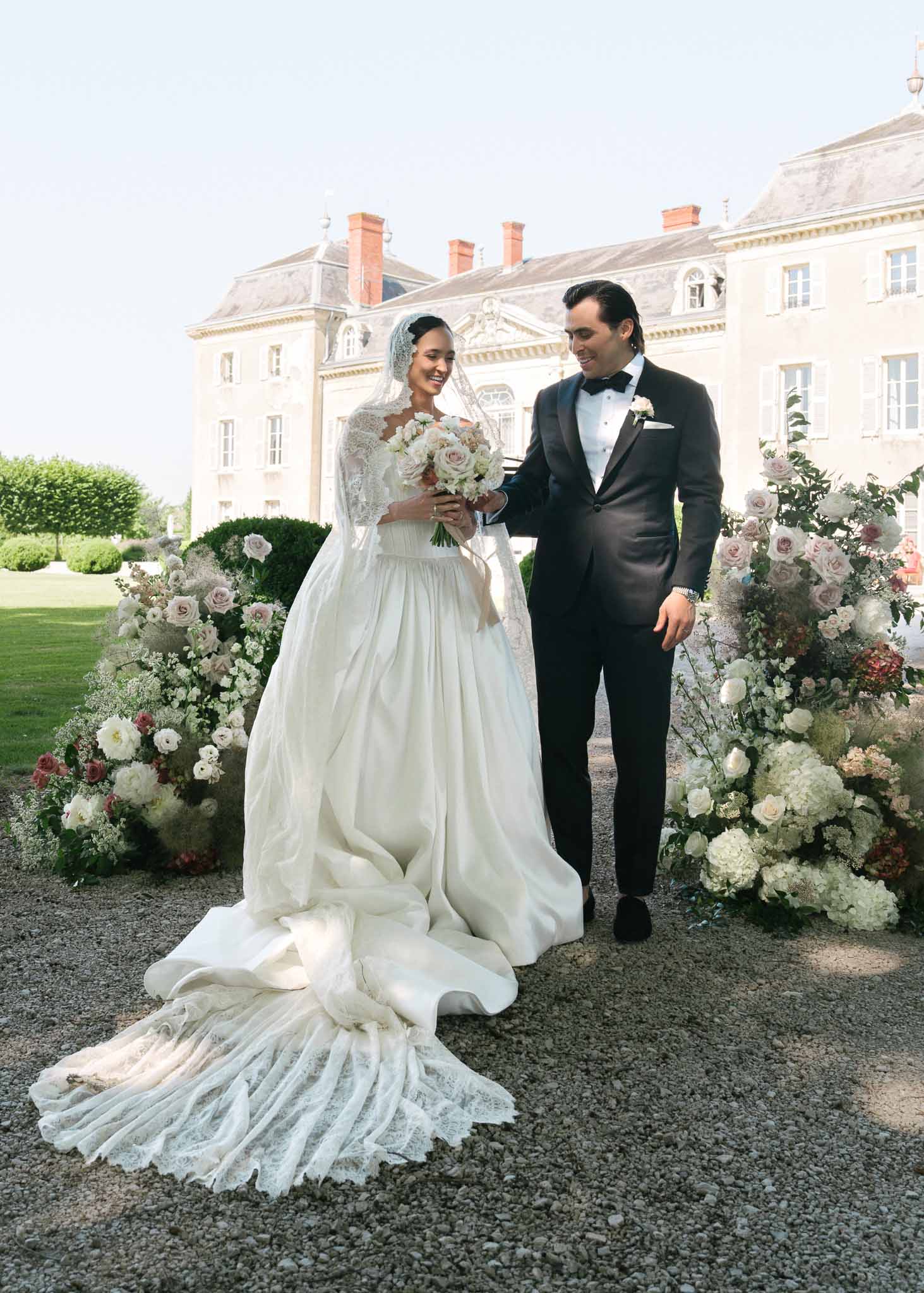 Couple between floral corridor of white hydrangeas and blush roses bride in lace gown with cathedral veil