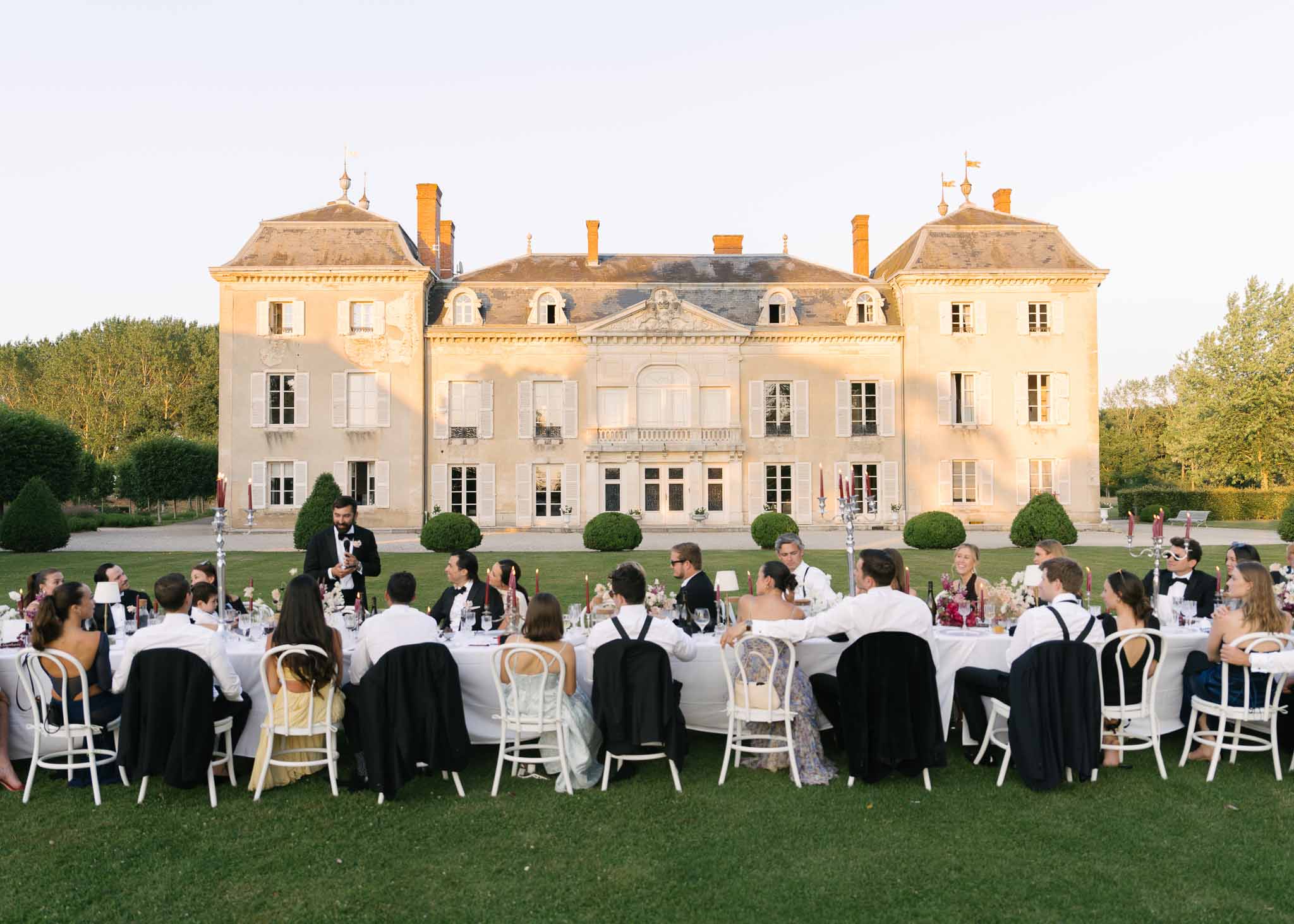 Golden hour outdoor reception dinner for 40 guests at long tables in front of 18th-century French chateau