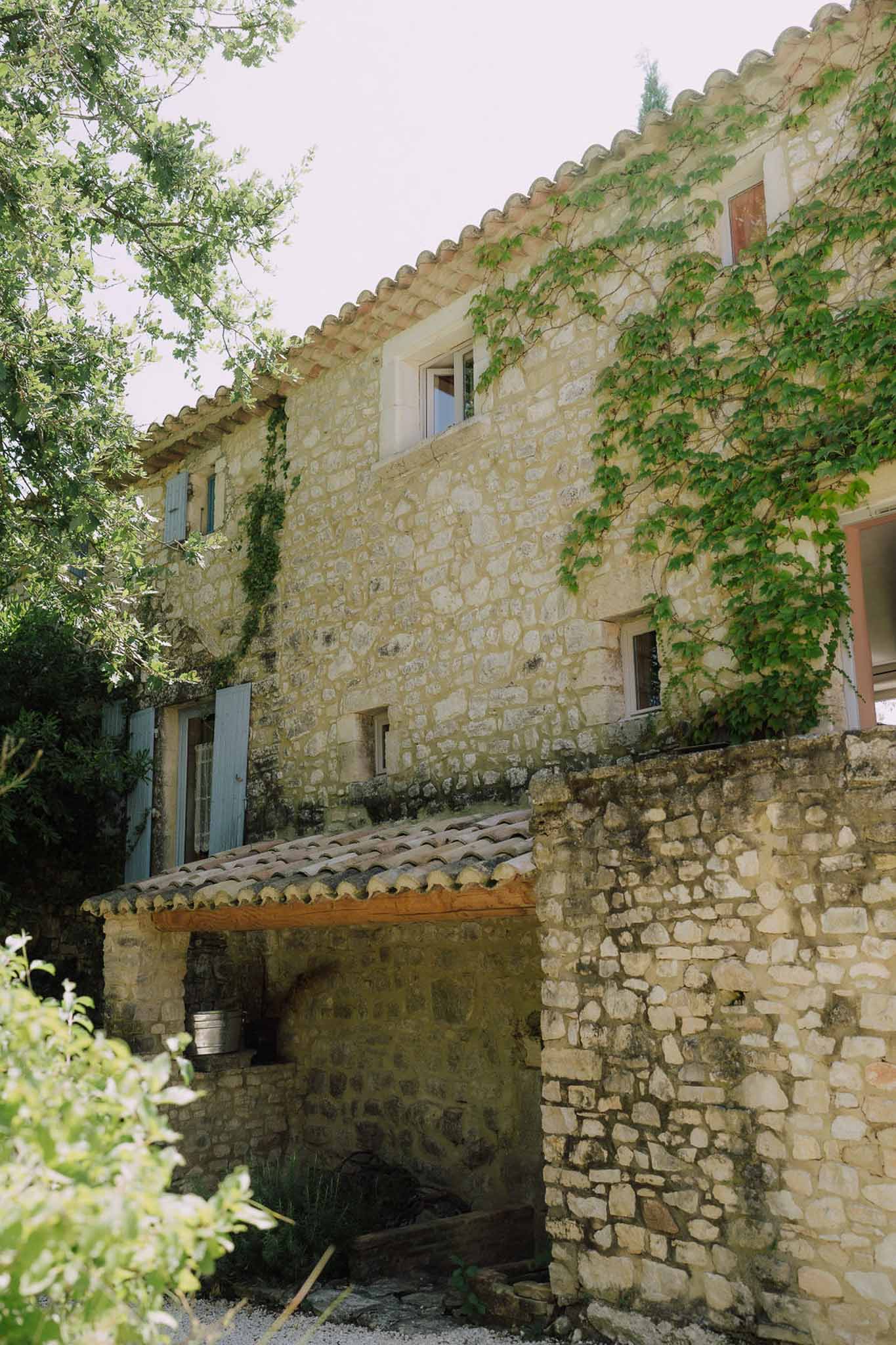 Provencal stone mas with honey limestone terracotta tiles blue-grey shutters and climbing vines in diffused light