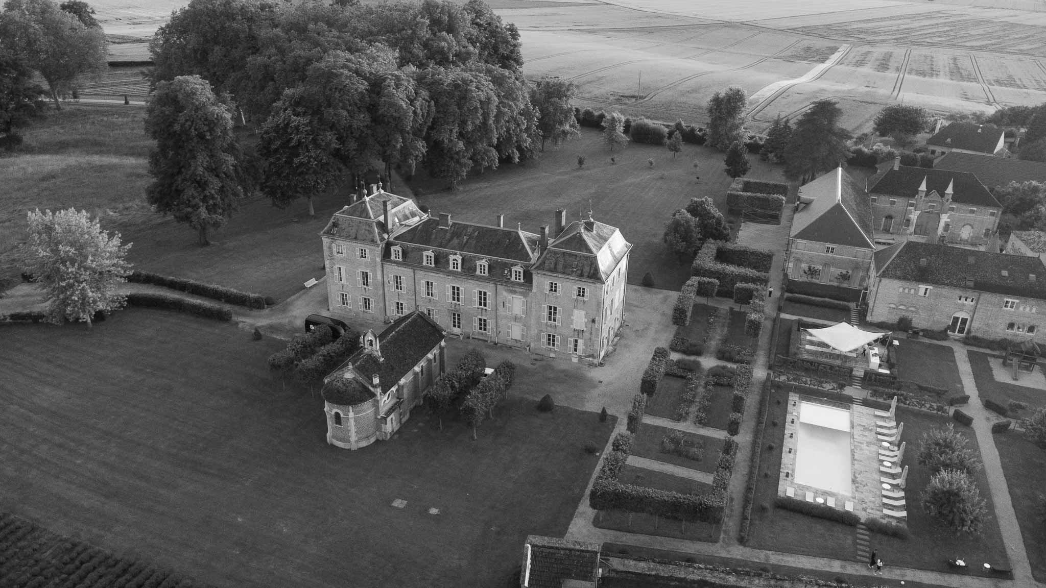 Aerial view of chateau estate with parterre gardens, pool, gatehouse turret, and farmland in B&W