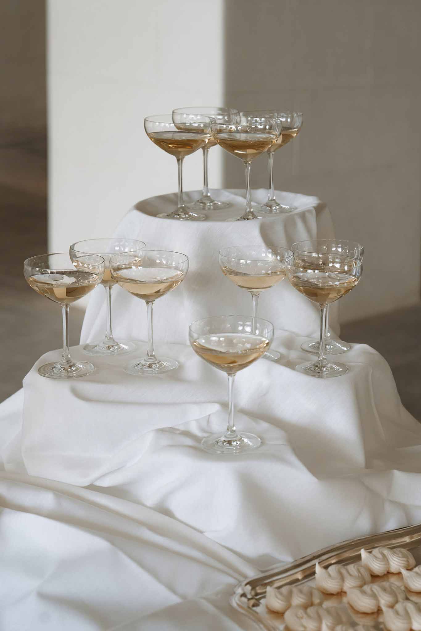 Rose champagne coupe tower with white meringues on silver tray against cream backdrop