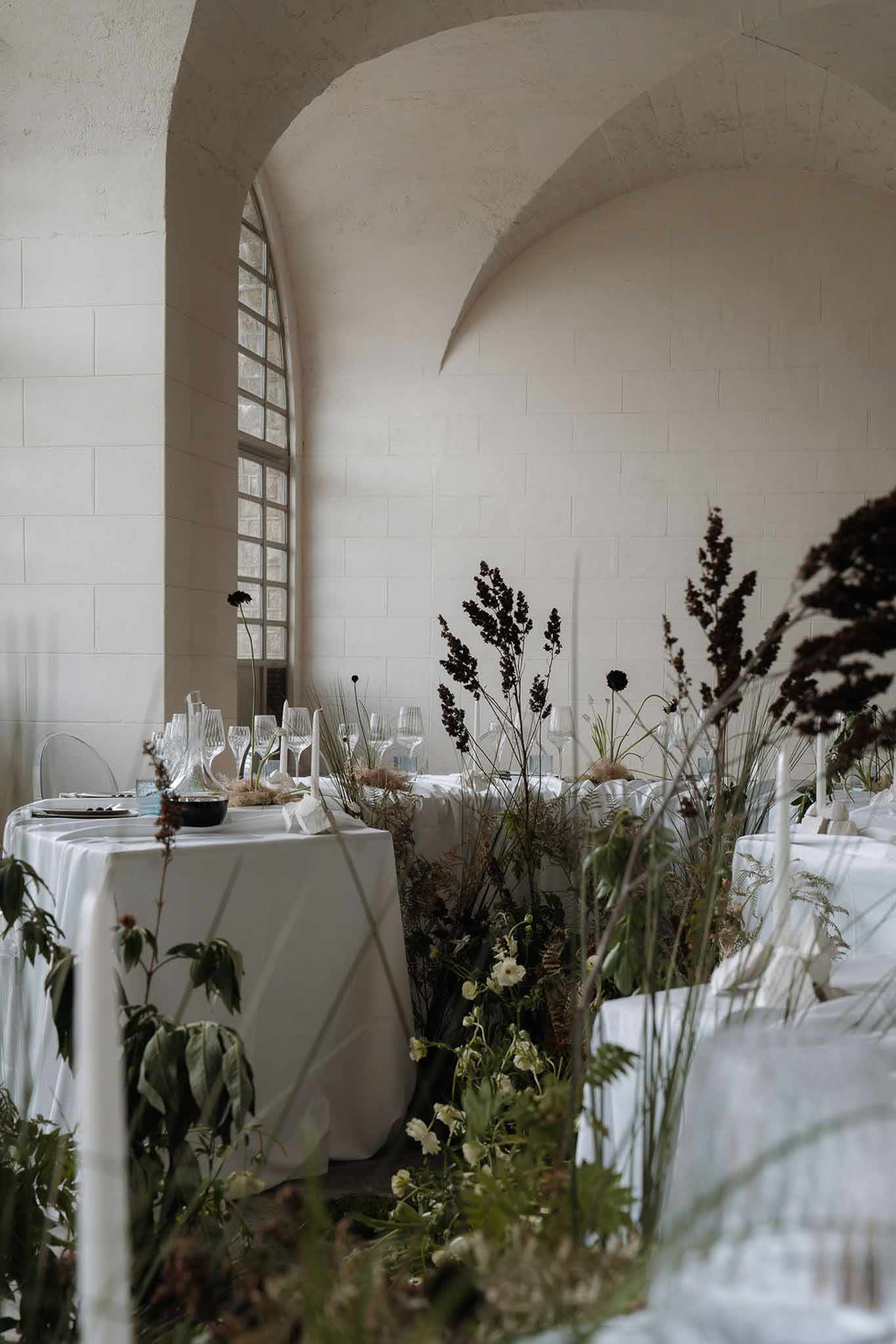Reception tables in vaulted stone hall with wild fern and dried grass arrangements creating a meadow effect