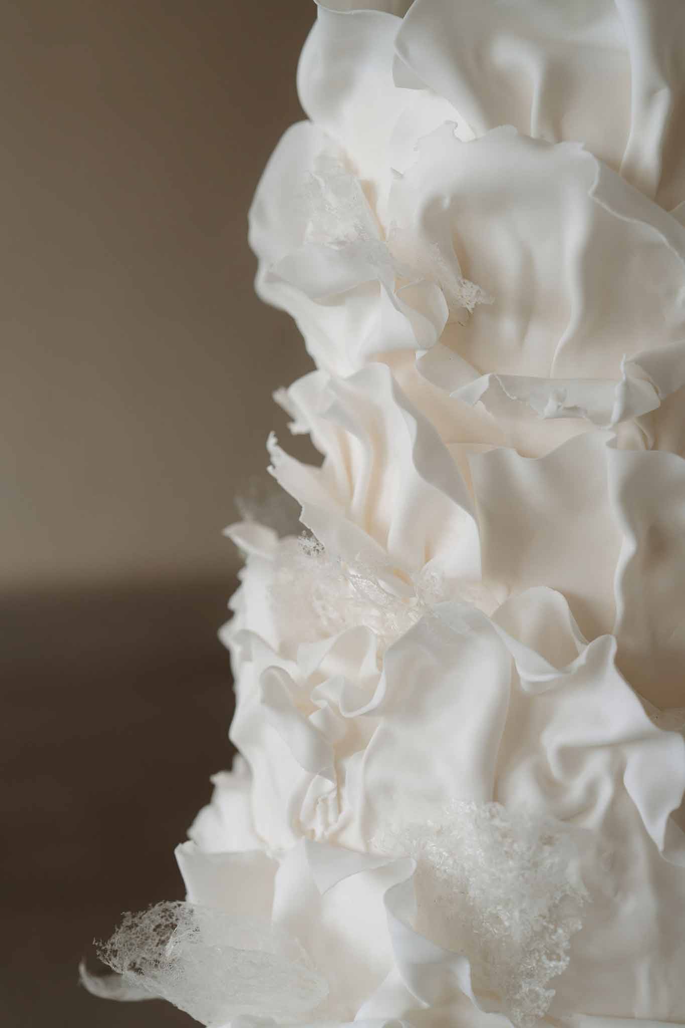 Multi-tier wedding cake decorated with layered ivory and white fondant ruffles and sugar crystal accents