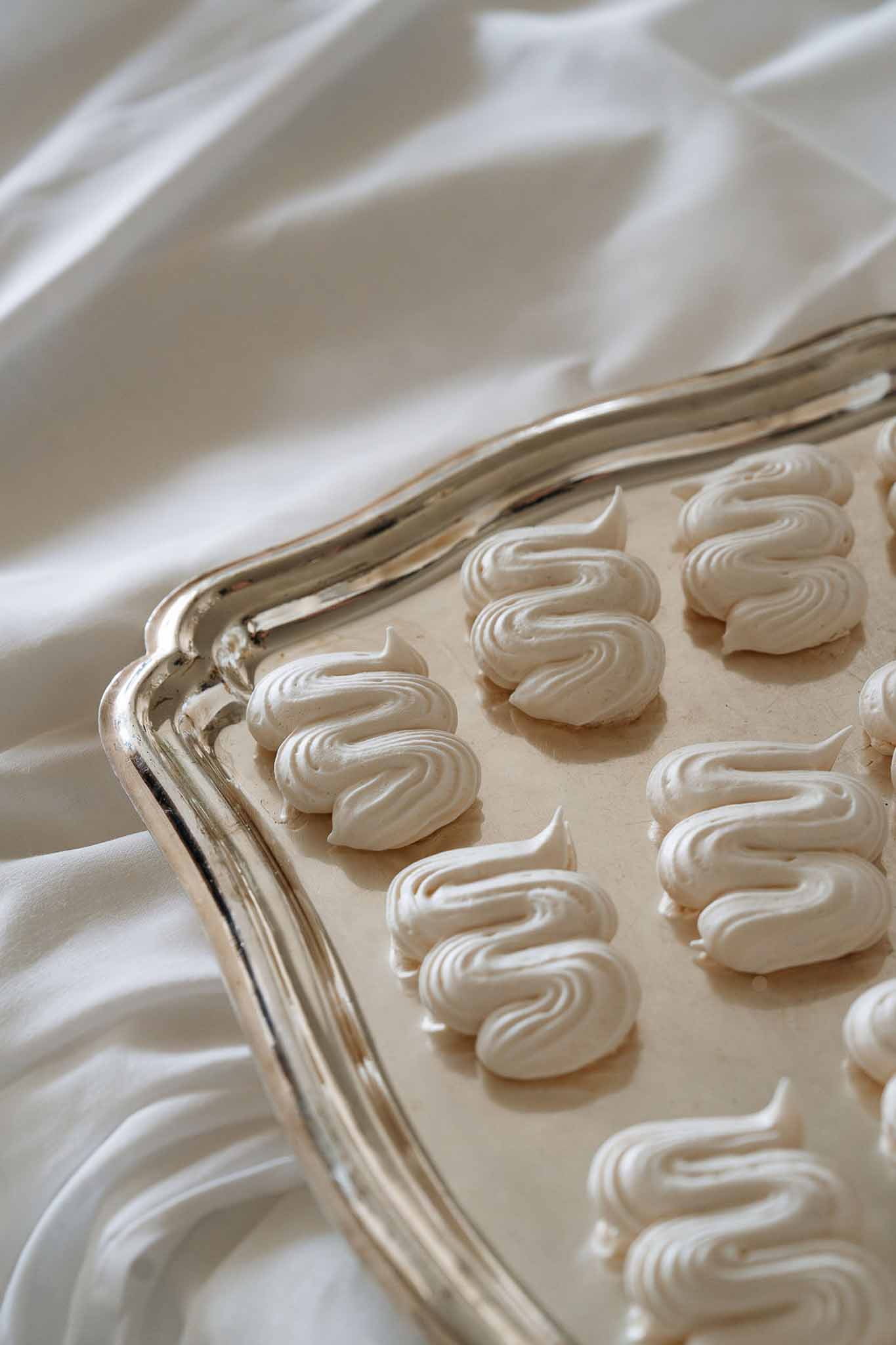 Ivory swirled meringue cookies arranged on ornate silver scalloped tray draped with white fabric