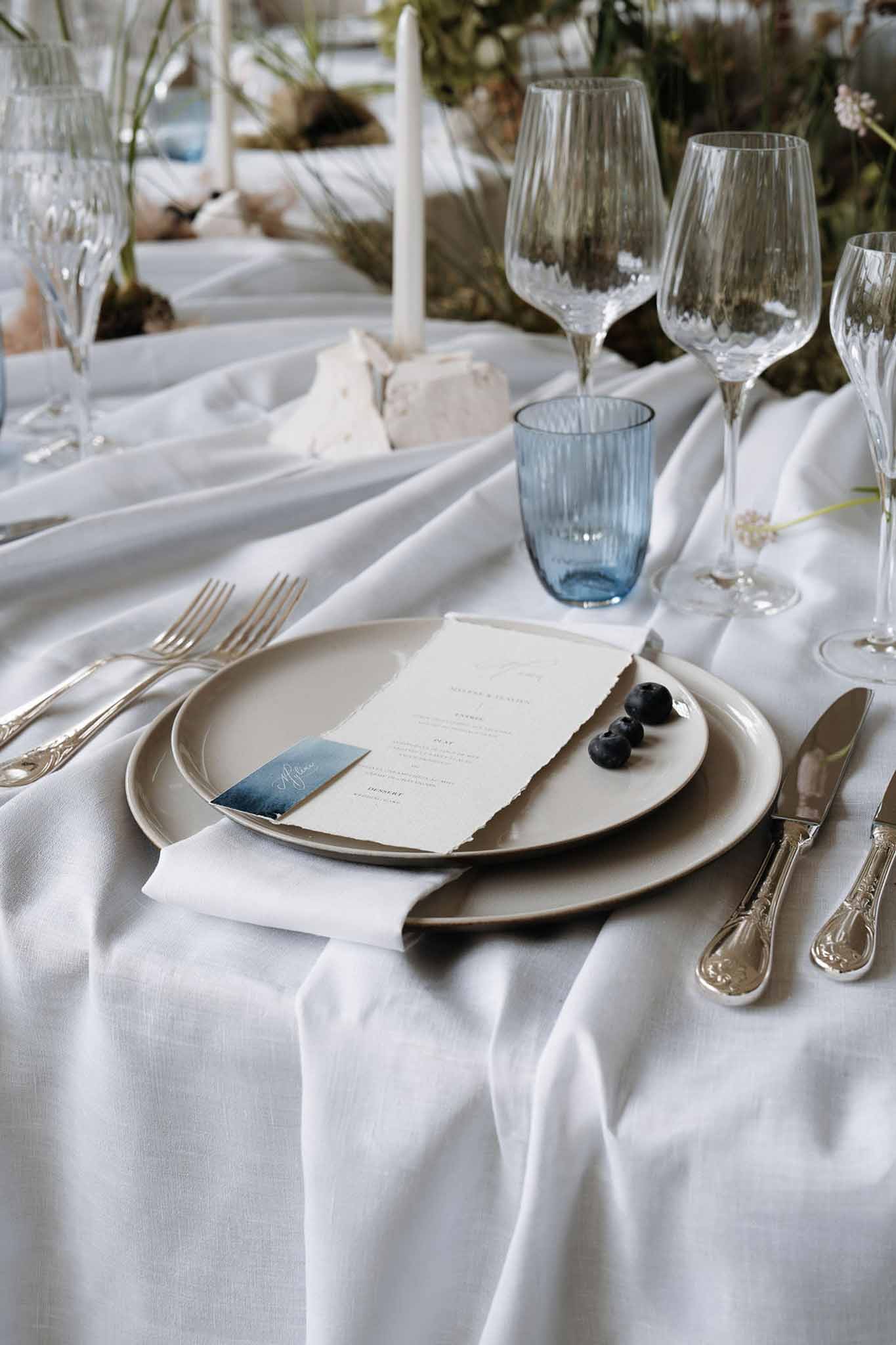 Place setting with greige plates, blue watercolor name card, ribbed dusty blue tumbler, and blueberry accent