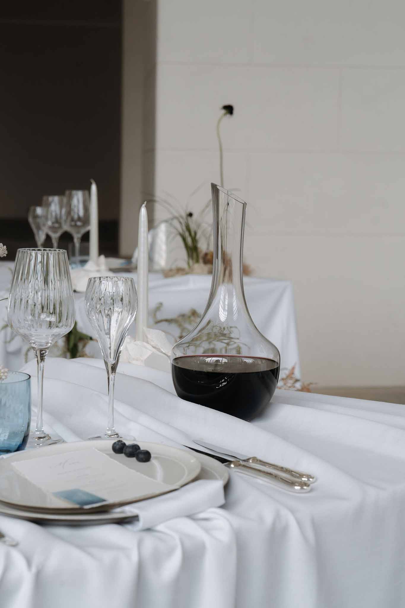 Minimalist place setting with stacked ceramic plates, blueberry garnish, and dusty blue glassware