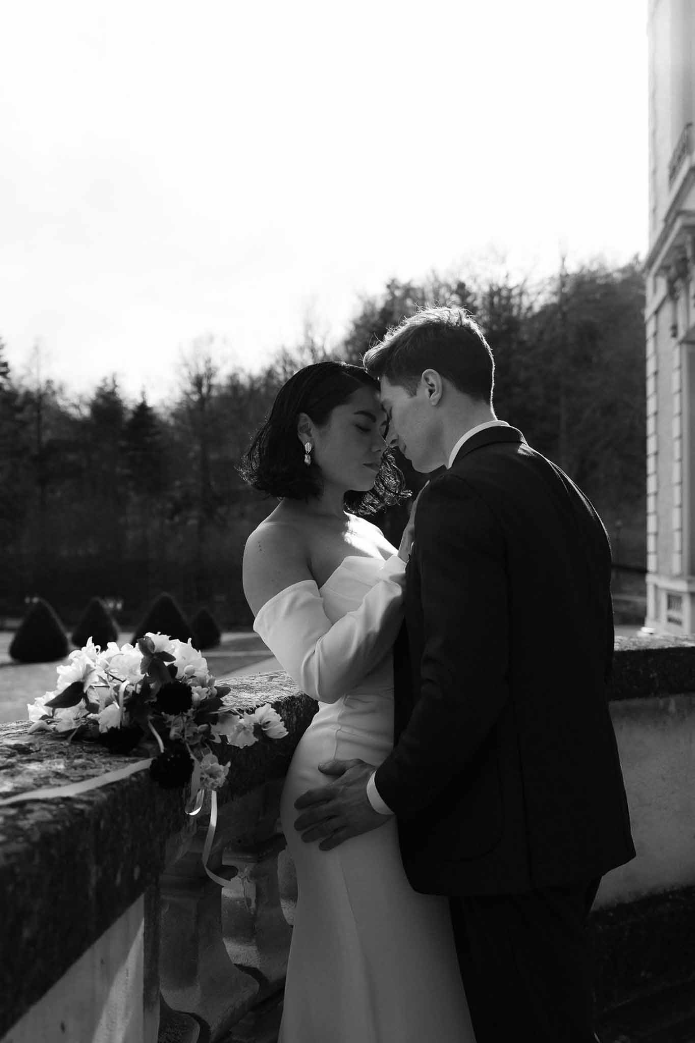 Black and white couple leaning foreheads together on stone balustrade terrace with garden topiary