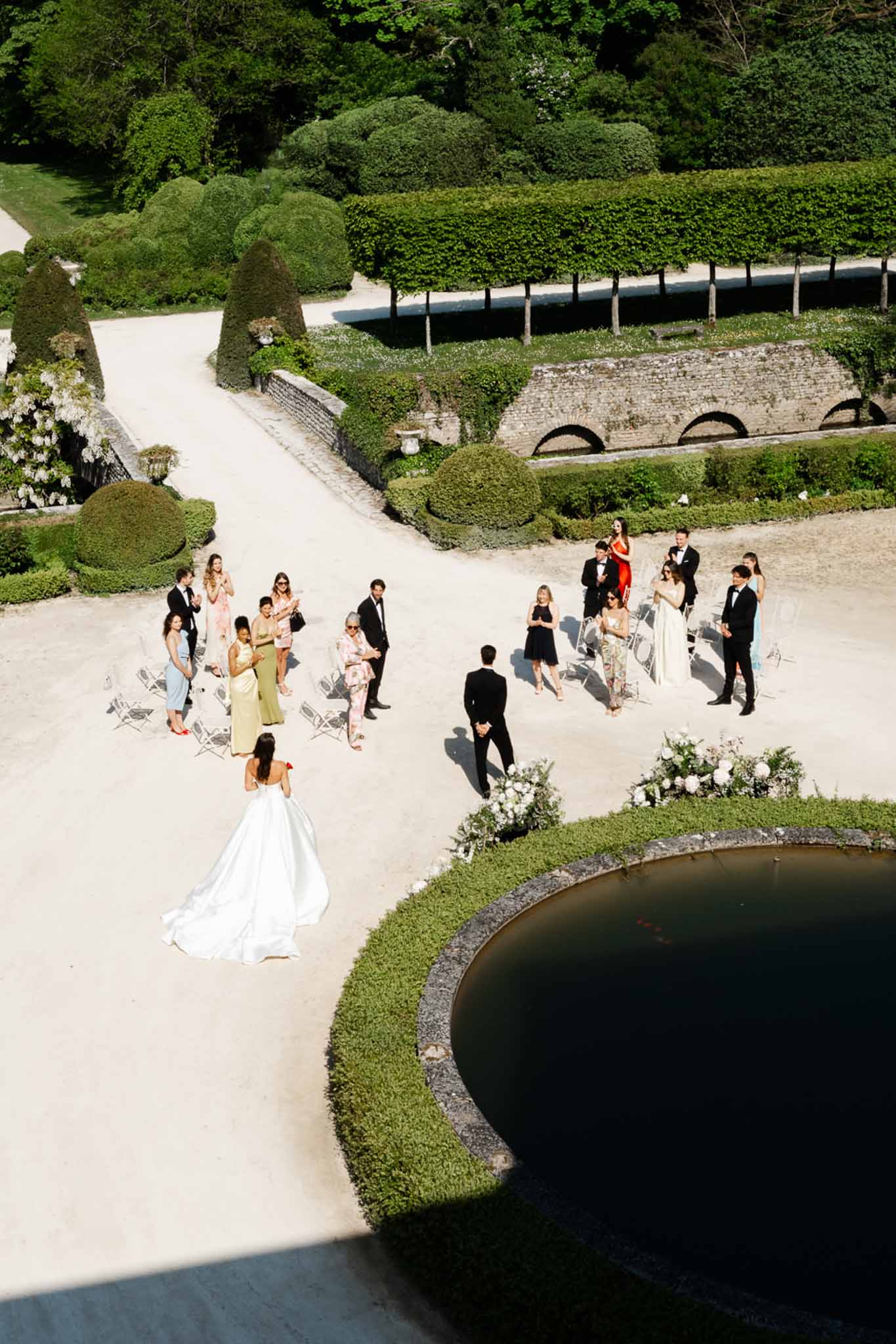Aerial view of ceremony in formal French garden with circular pond topiary and seated guests