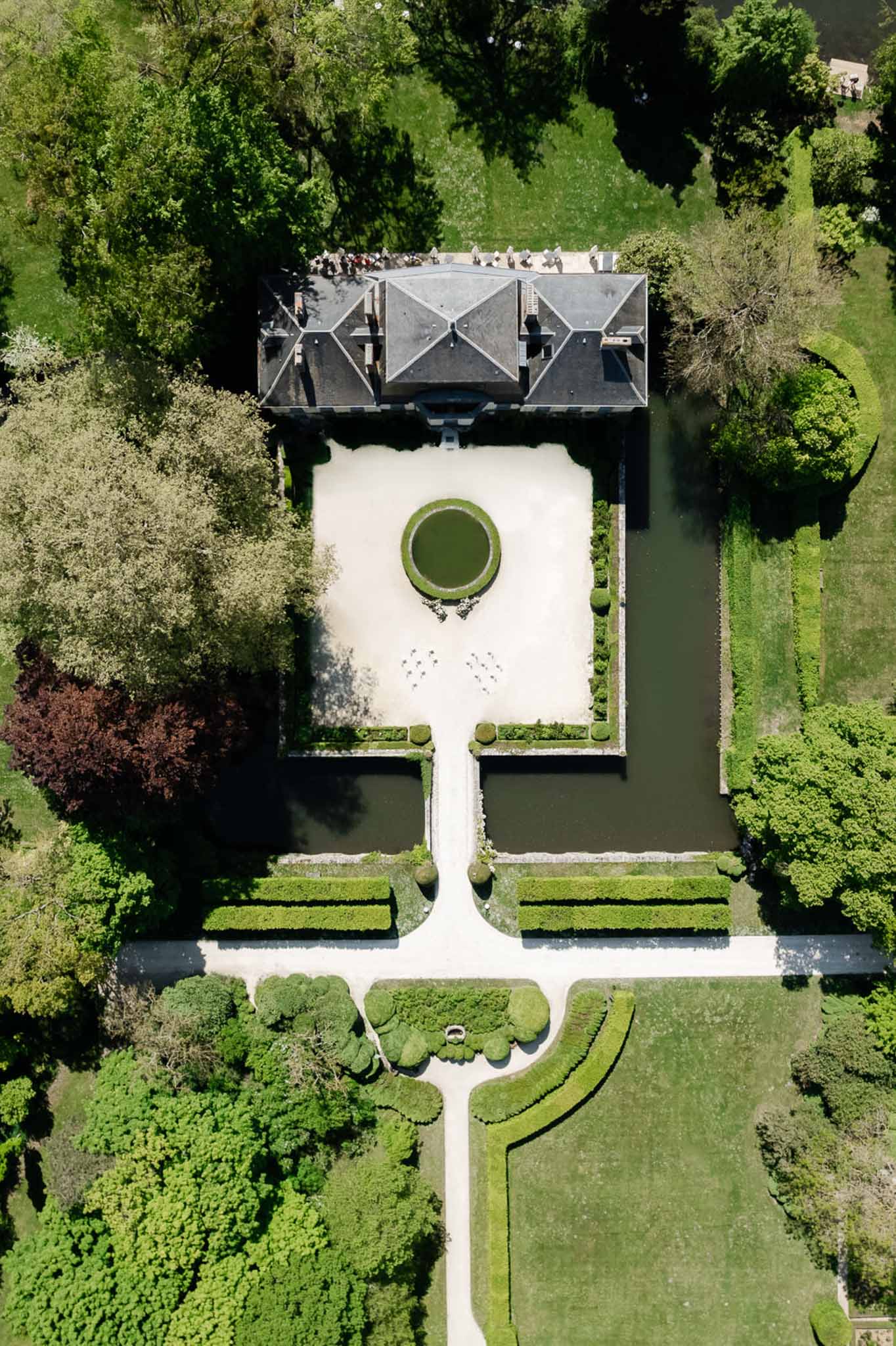 Aerial drone view of French chateau with slate mansard roof, rectangular moat, and formal parterre gardens