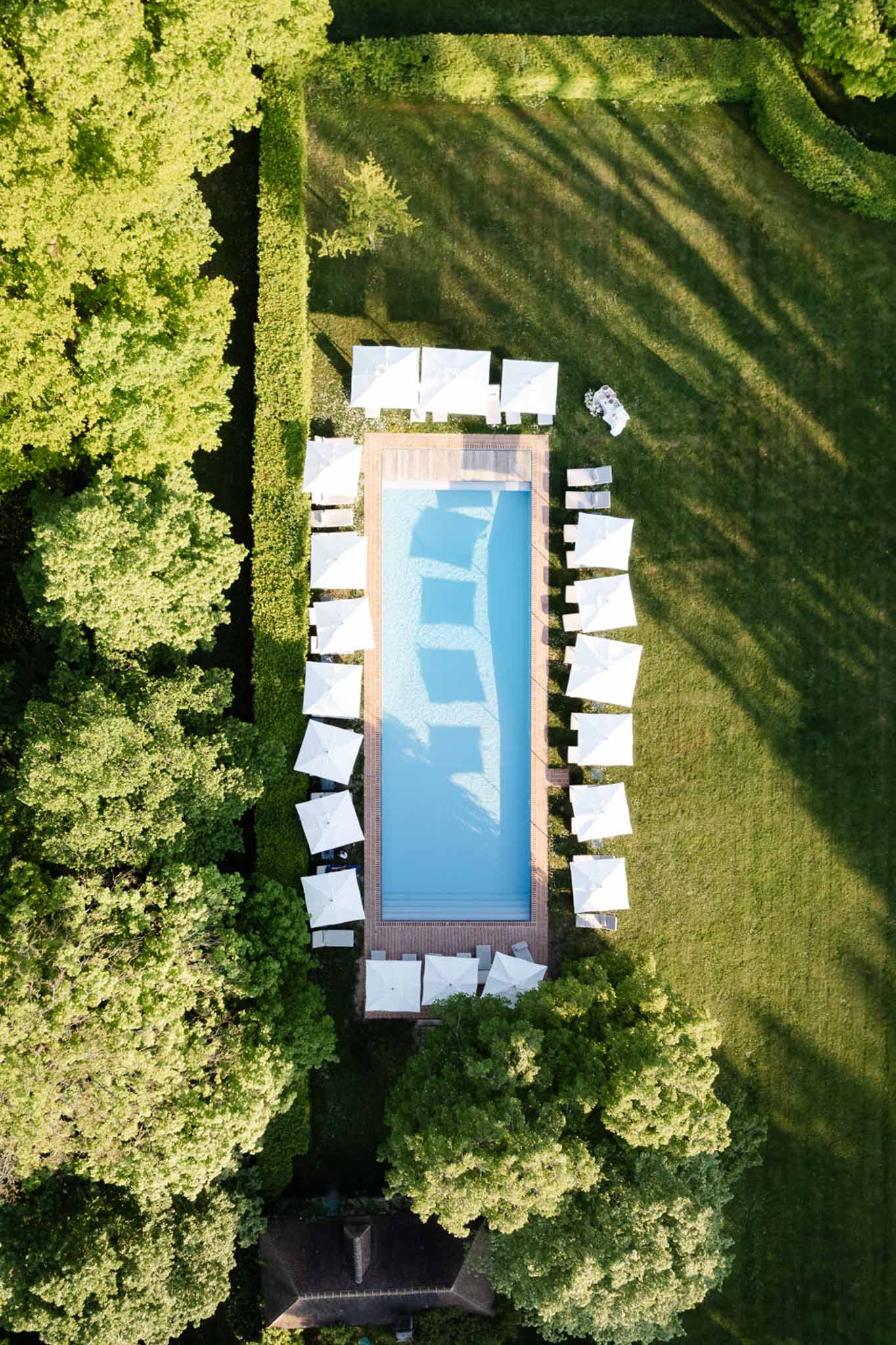 Aerial view of rectangular pool with white parasols and sun loungers on estate grounds