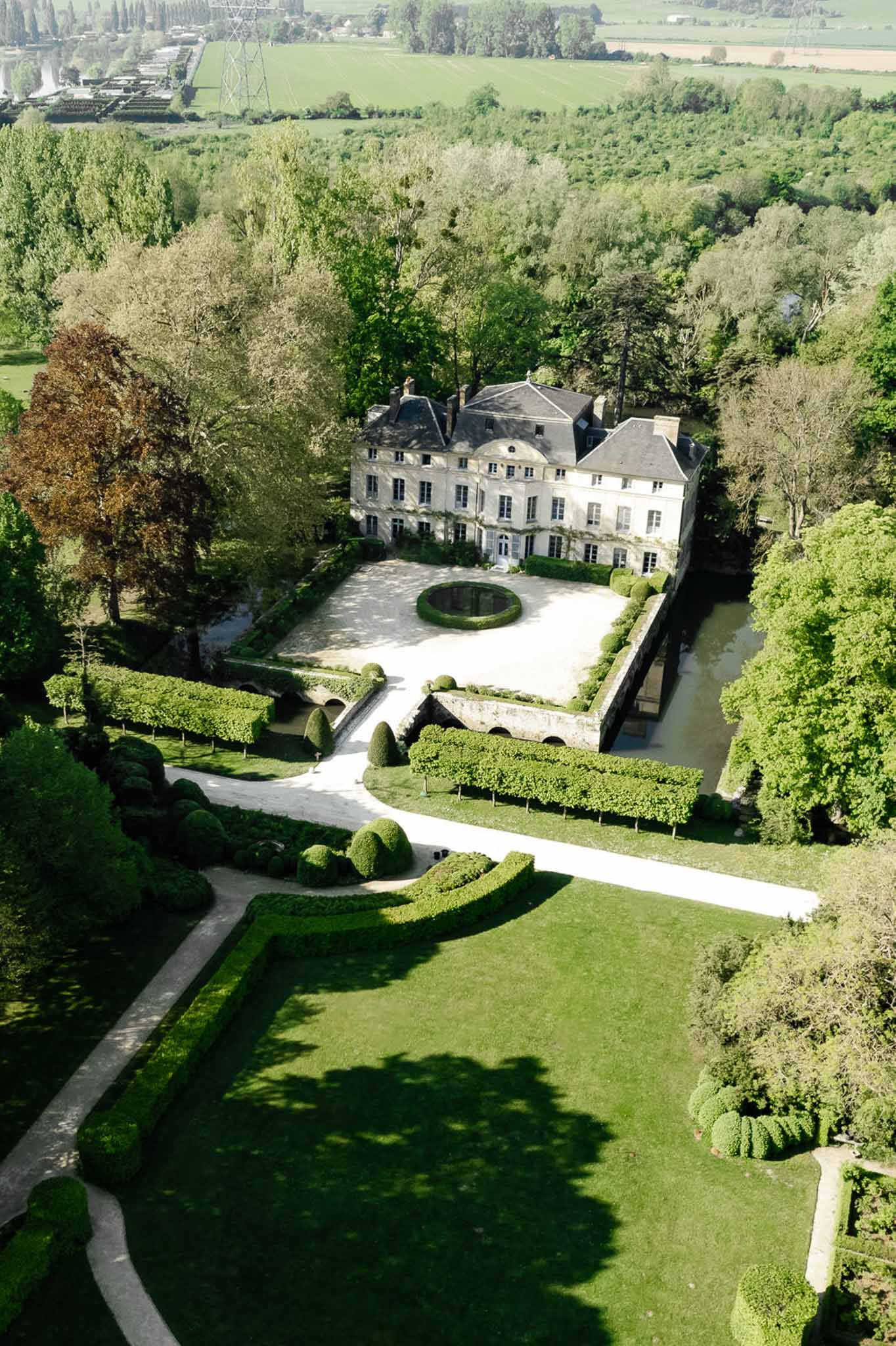 Aerial view of French chateau with reflecting pool, moat, formal boxwood gardens, and mature tree grounds