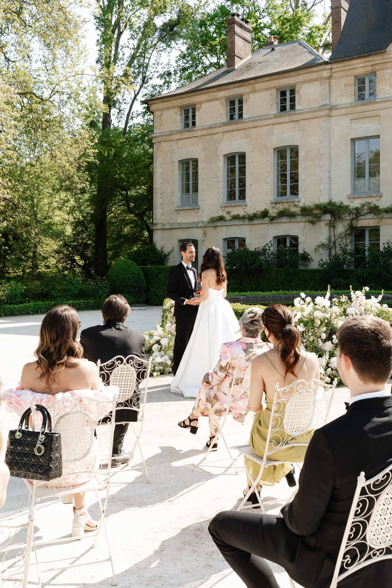 Intimate six-guest ceremony on gravel courtyard with blush floral shrubs before cream limestone chateau