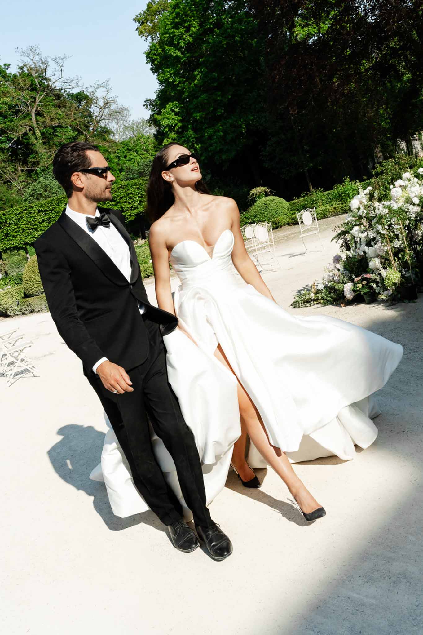 Bride and groom in matching black sunglasses with billowing skirt in formal garden setting