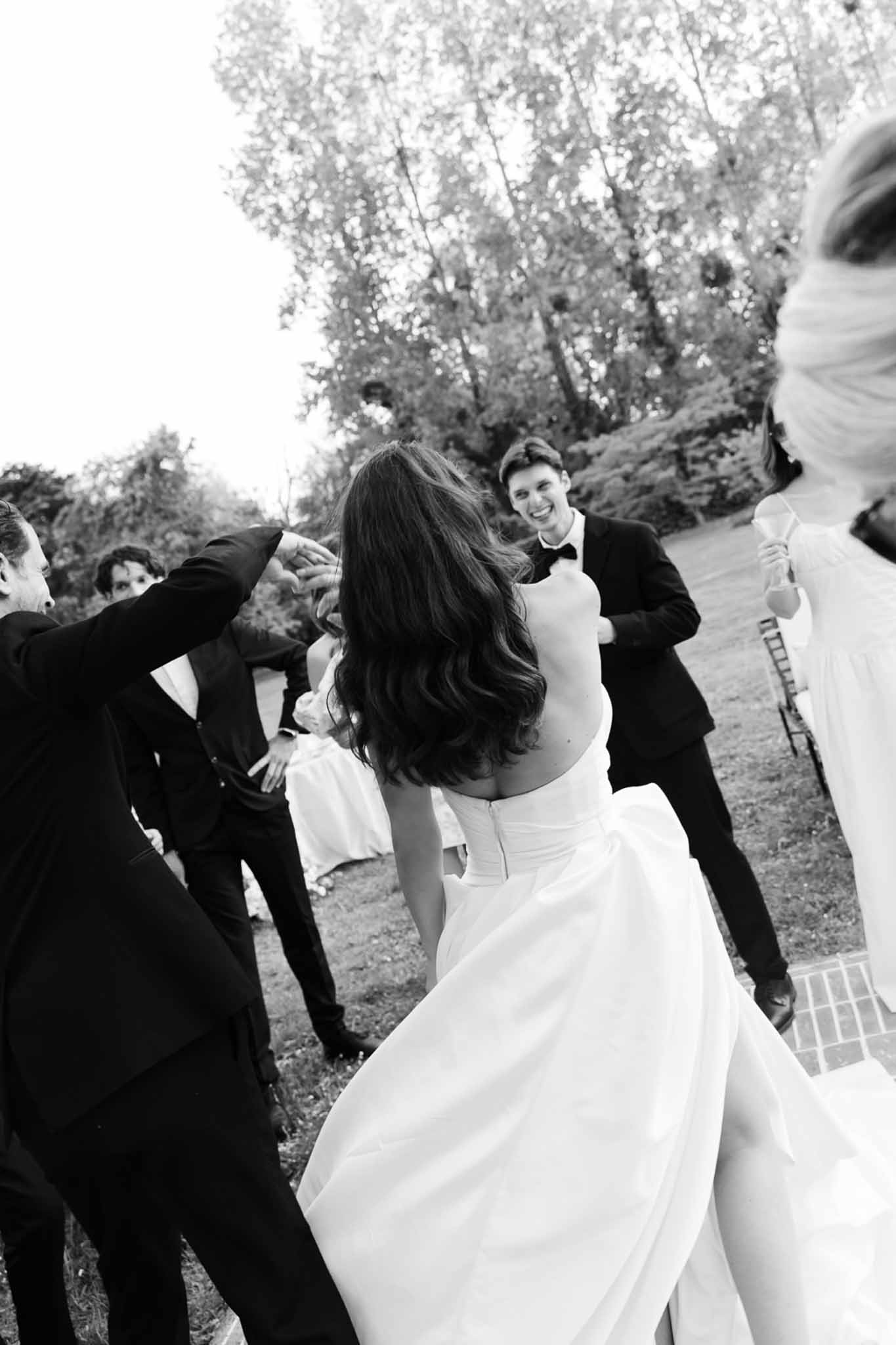 Black and white couple dancing surrounded by cheering guests with arms raised on lawn
