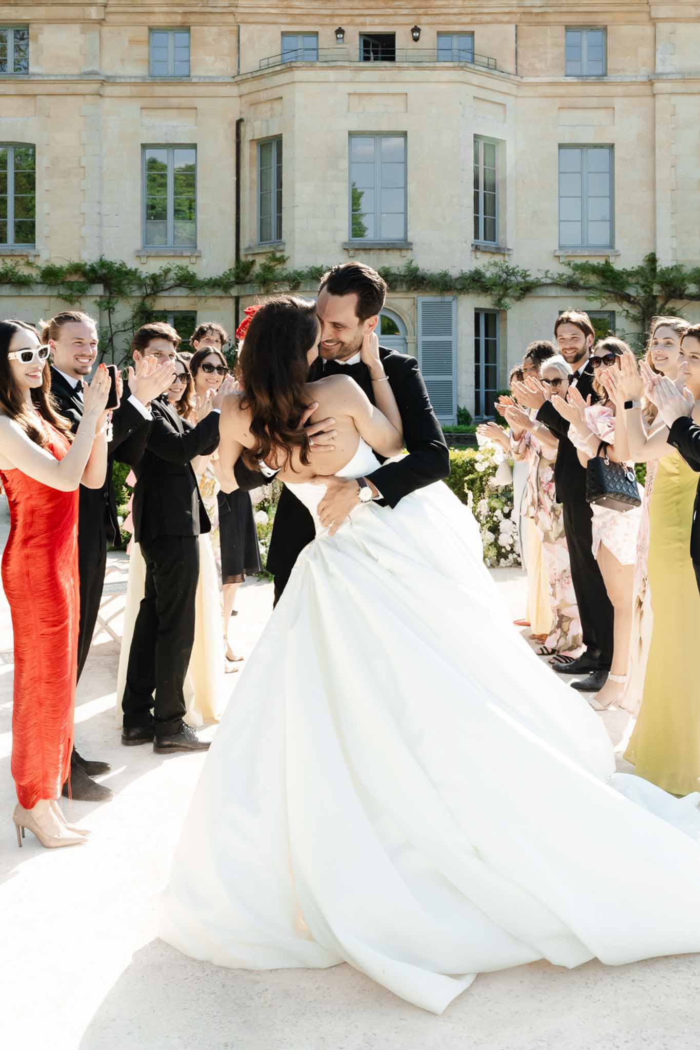 Bride and groom kiss in chateau courtyard as 15 guests clap and cheer on both sides