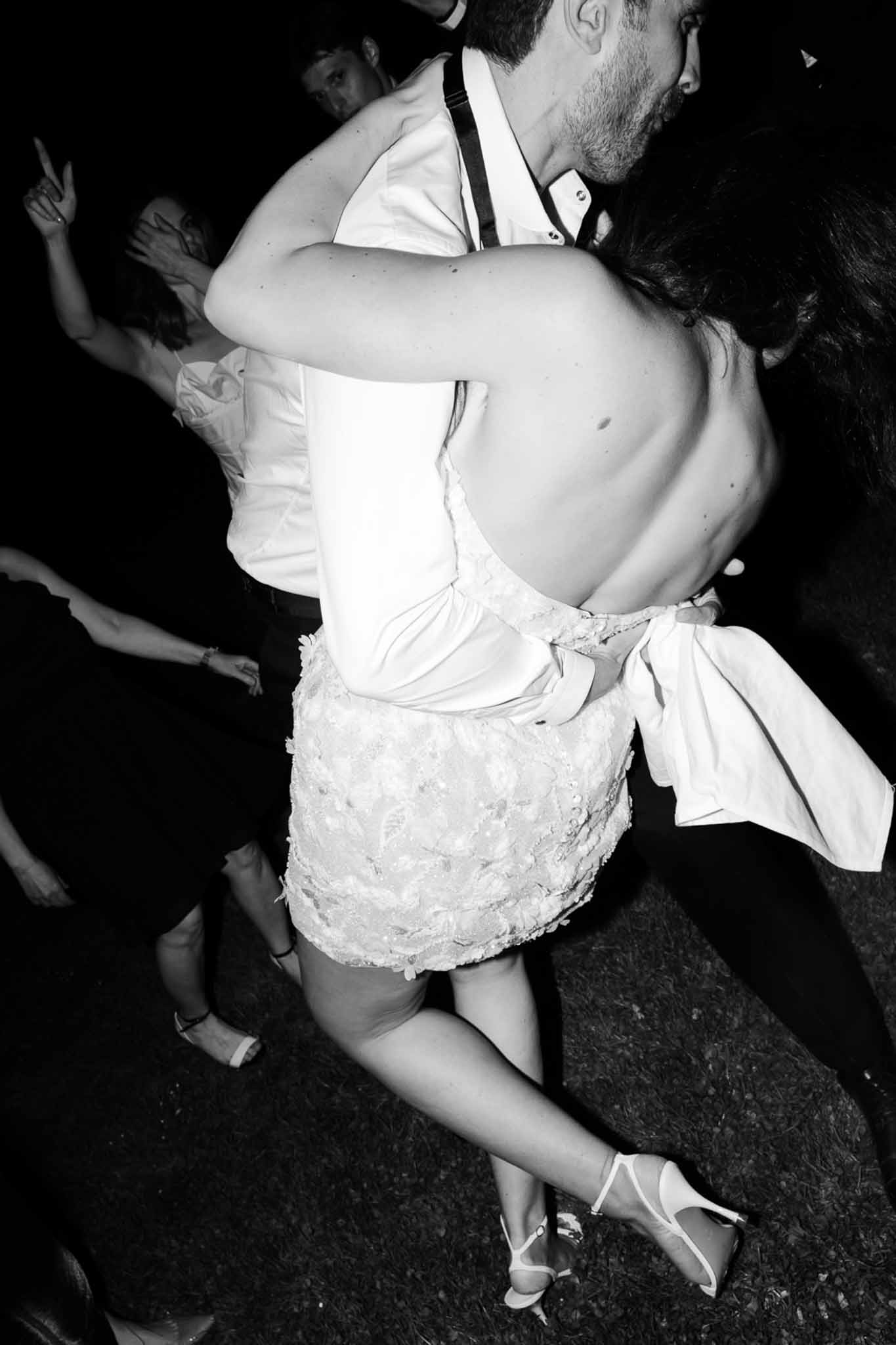 Black and white shot of bride in backless floral applique dress dancing with groom at night reception