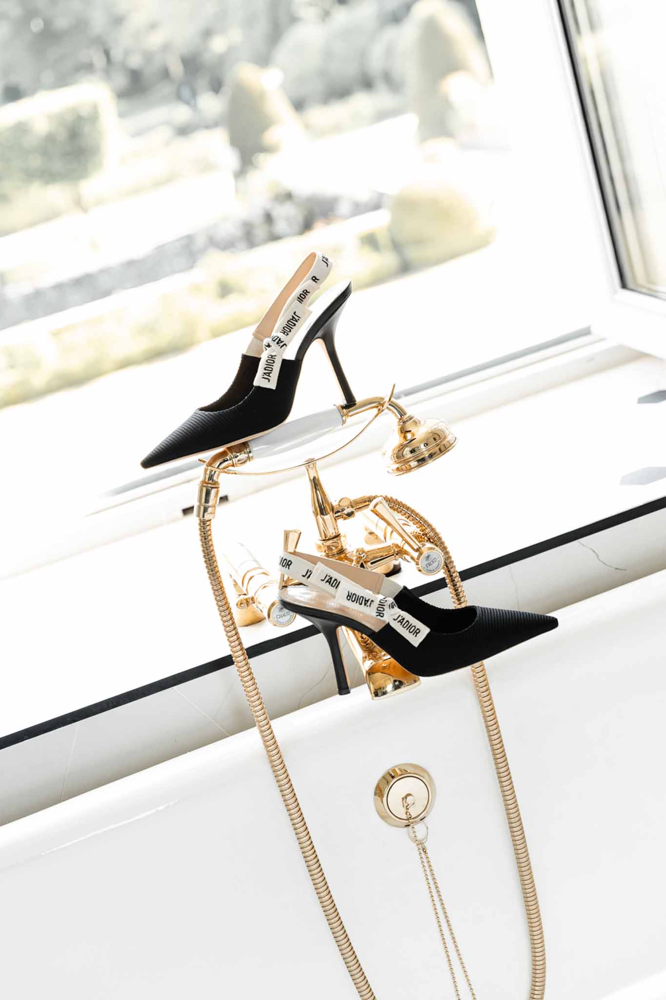 Black Dior J'Adior stiletto heels with white straps styled on white bathtub rim with gold hardware