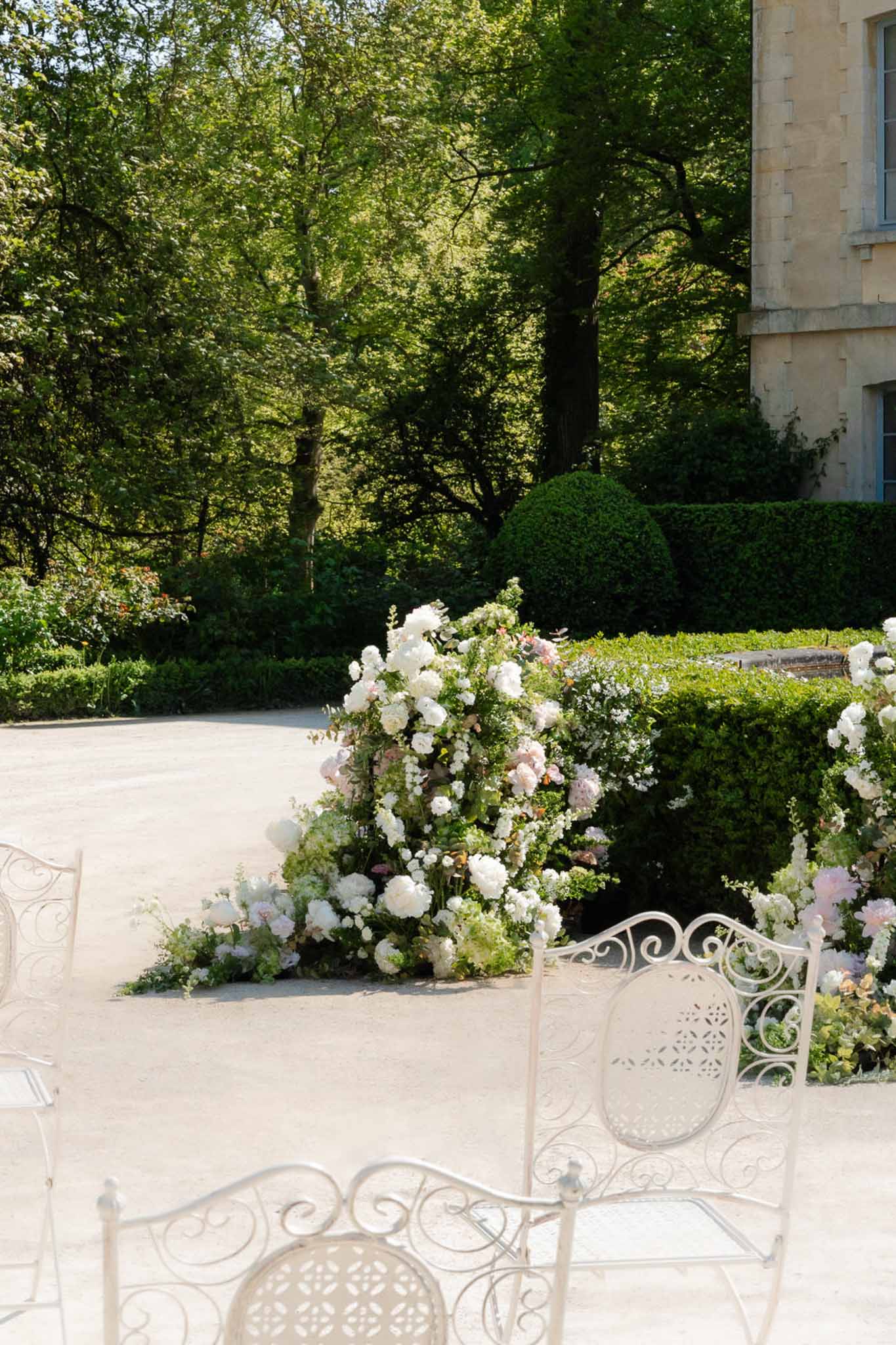 White wrought-iron chairs with peony and rose ground installation as altar marker at chateau courtyard
