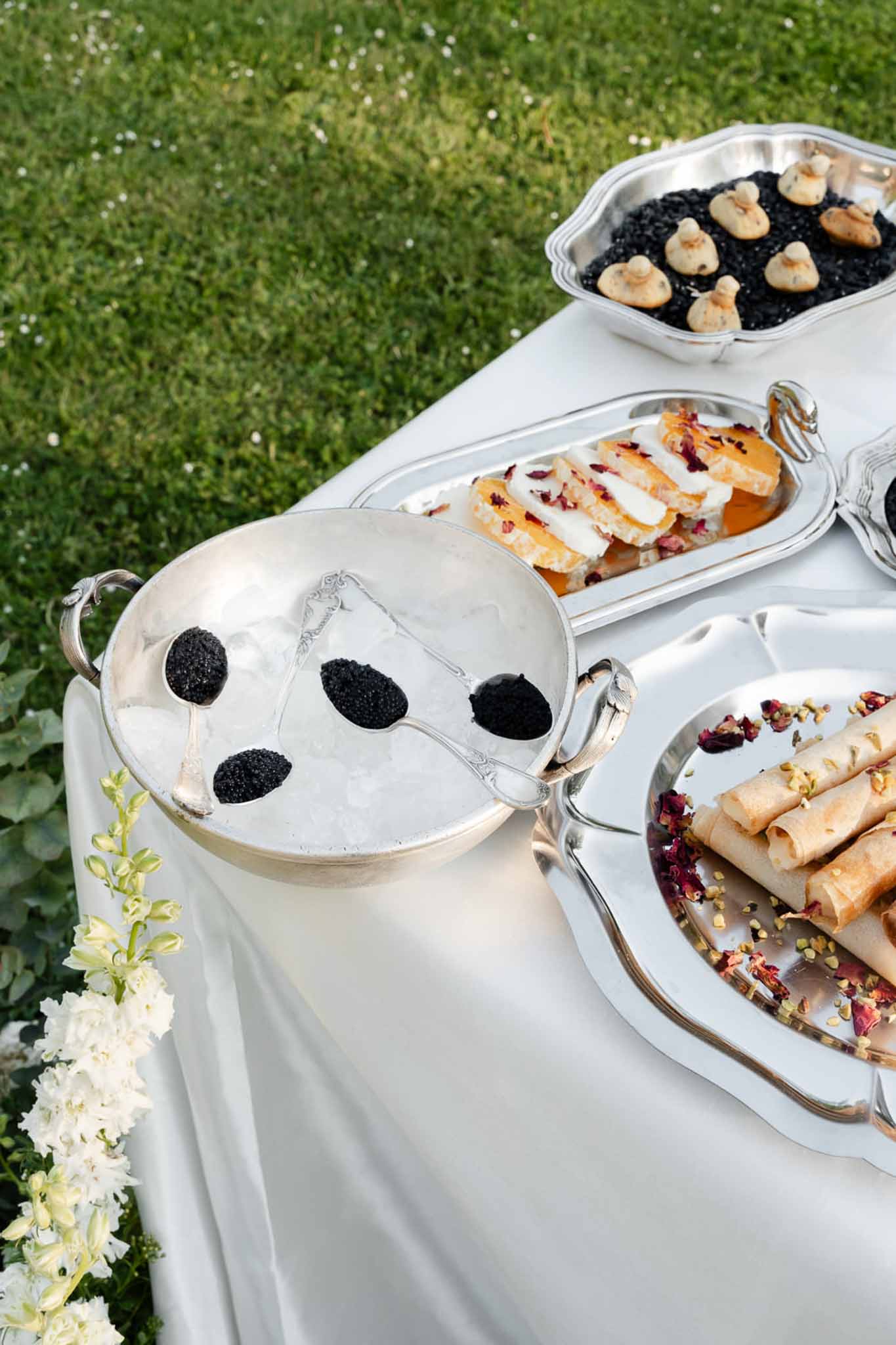 Silver trays with caviar on mother-of-pearl spoons, citrus canapes, rose petal crepes, and squid ink mousse