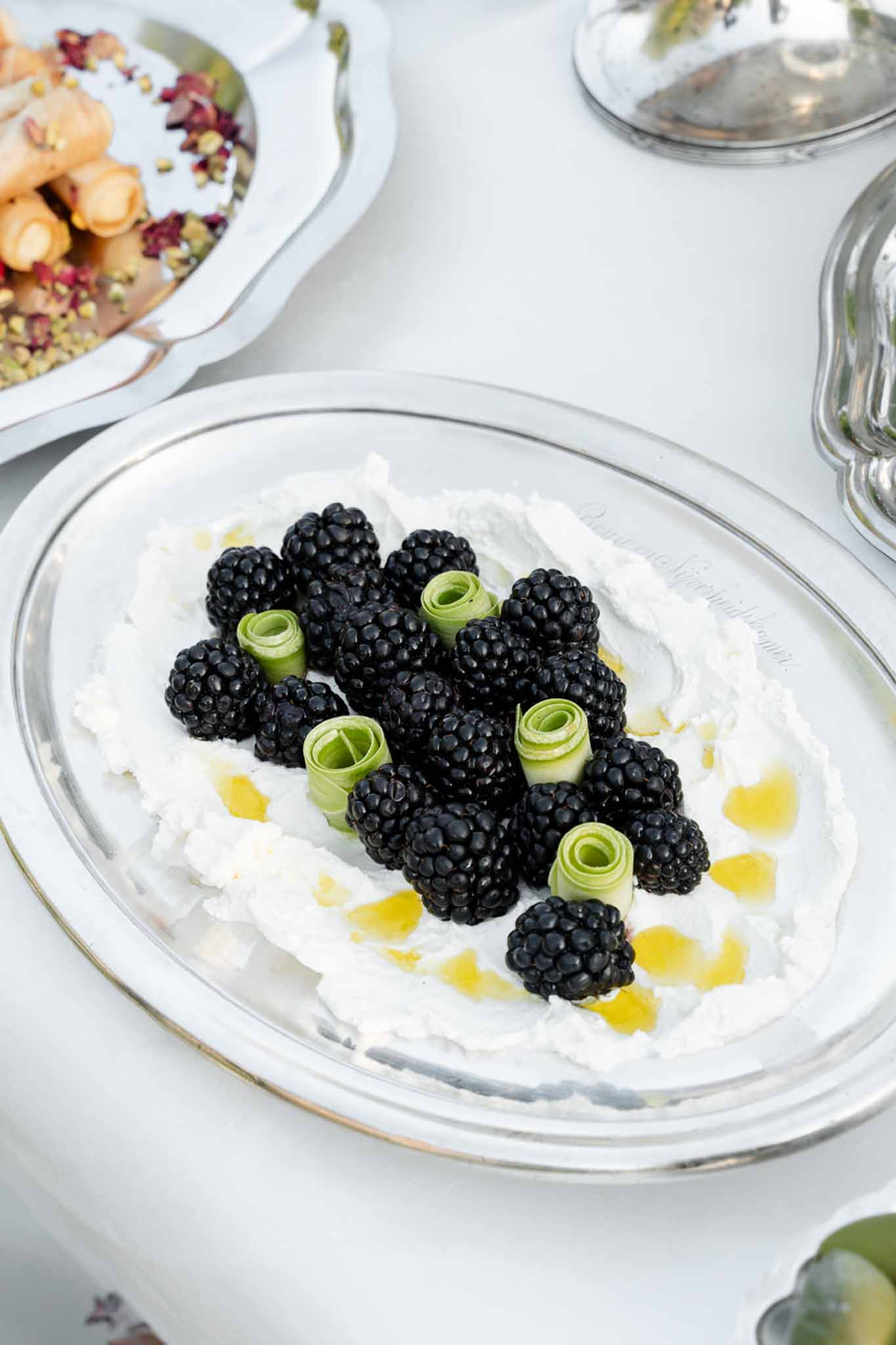 Silver serving dish with whipped cheese topped with blackberries and cucumber garnishes
