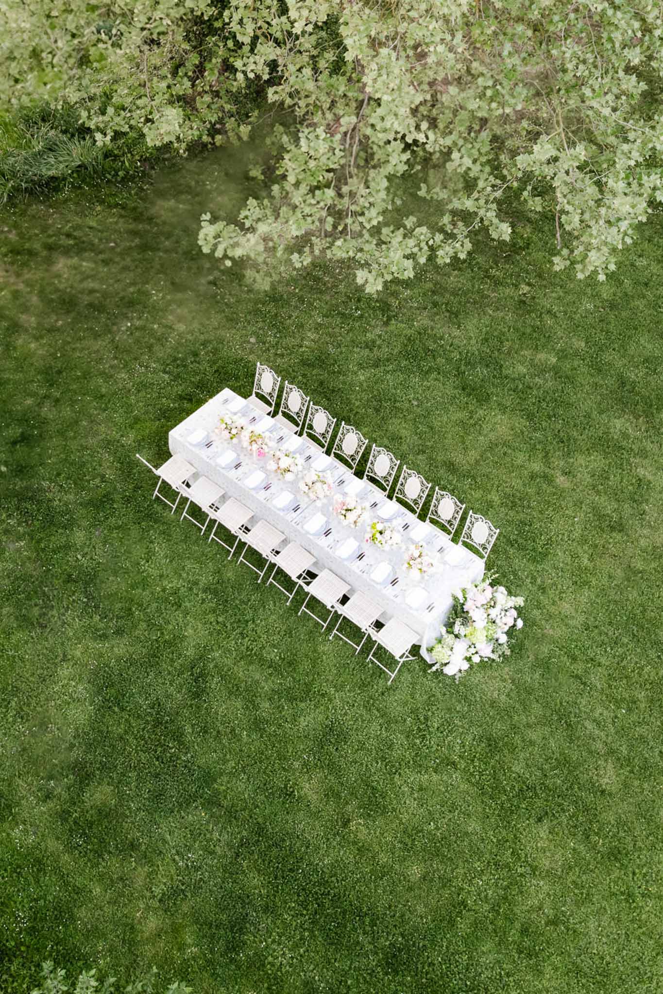 Aerial view of long outdoor reception table on lawn with pink and white floral centrepiece and white chairs