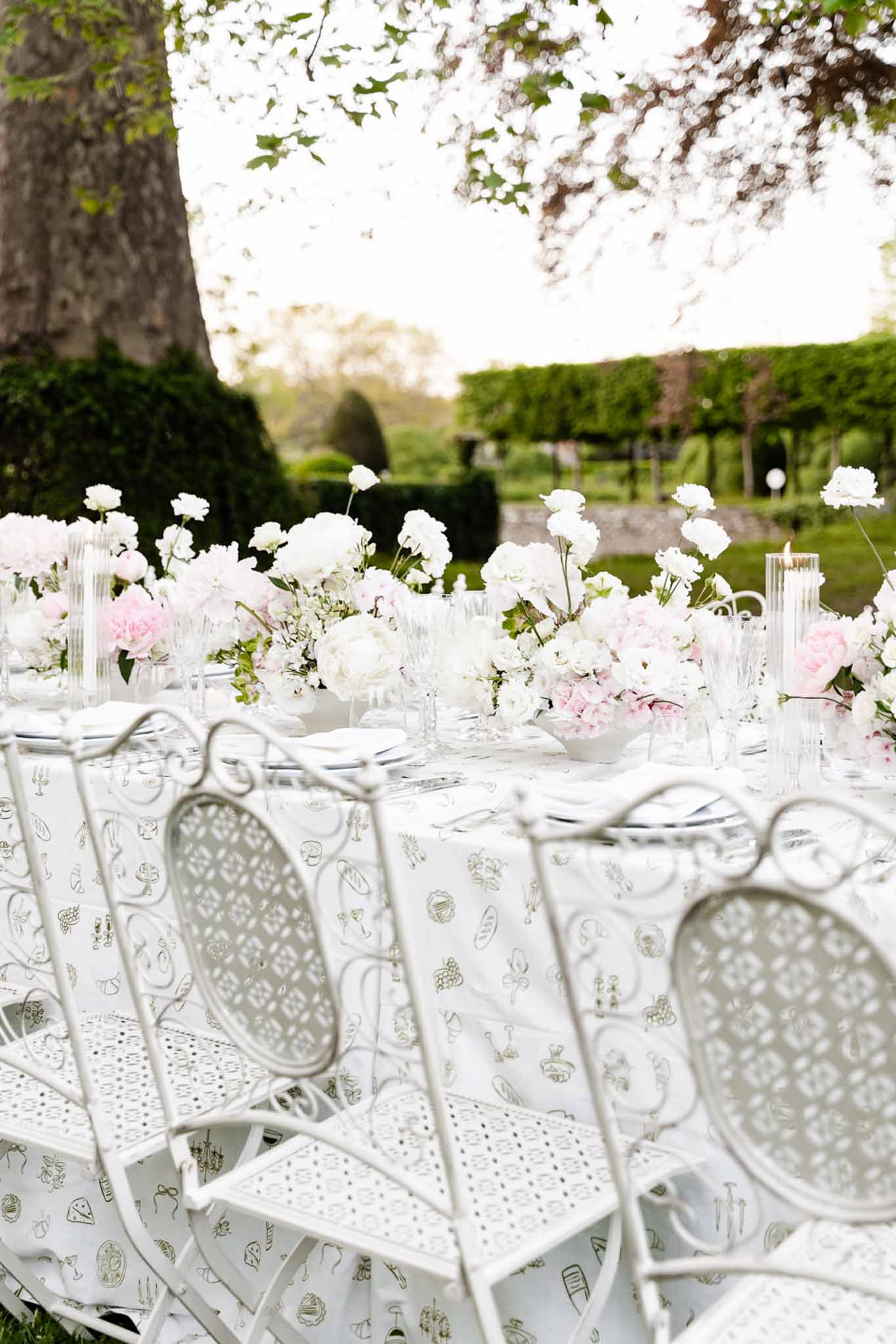 Long outdoor reception table with white peonies, blush pink flowers, and wrought-iron garden chairs