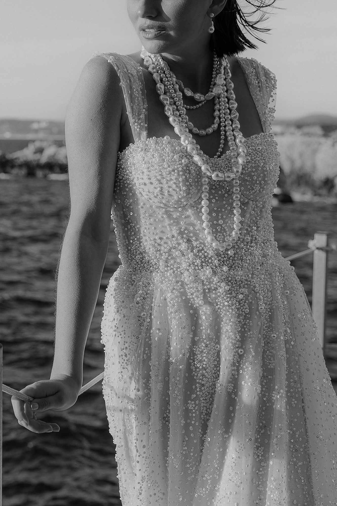 Black and white close-up of beaded bustier gown and layered pearl necklaces on bride