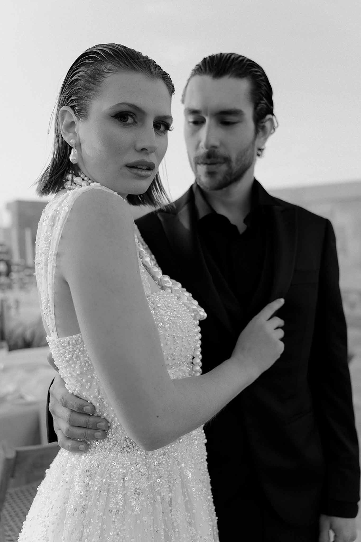 Bride in sequined gown with pearl choker and groom in black shirt in editorial close-up B&W