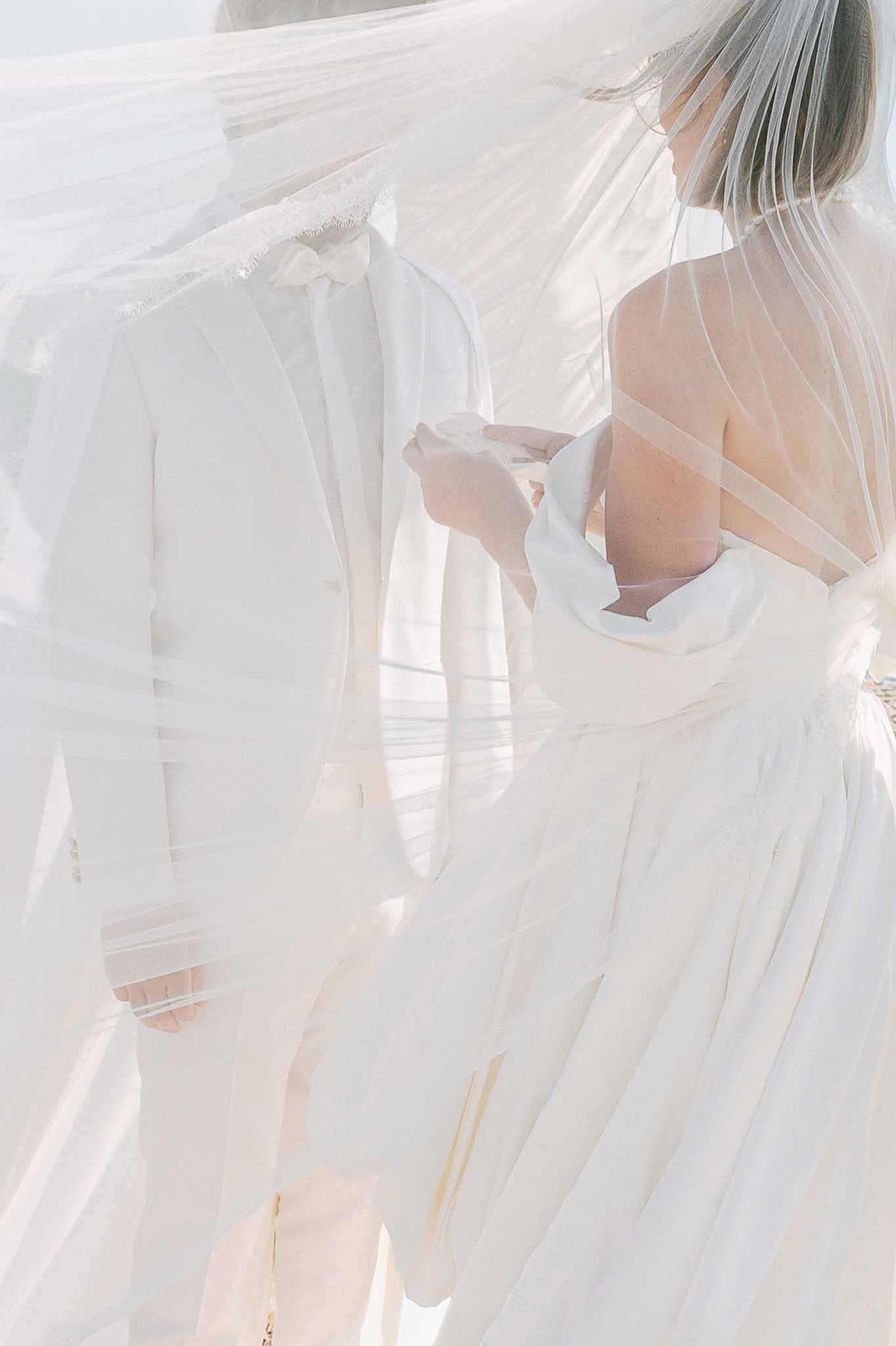 Bride and groom seen through billowing lace-edged veil in high-key close-up outdoor portrait