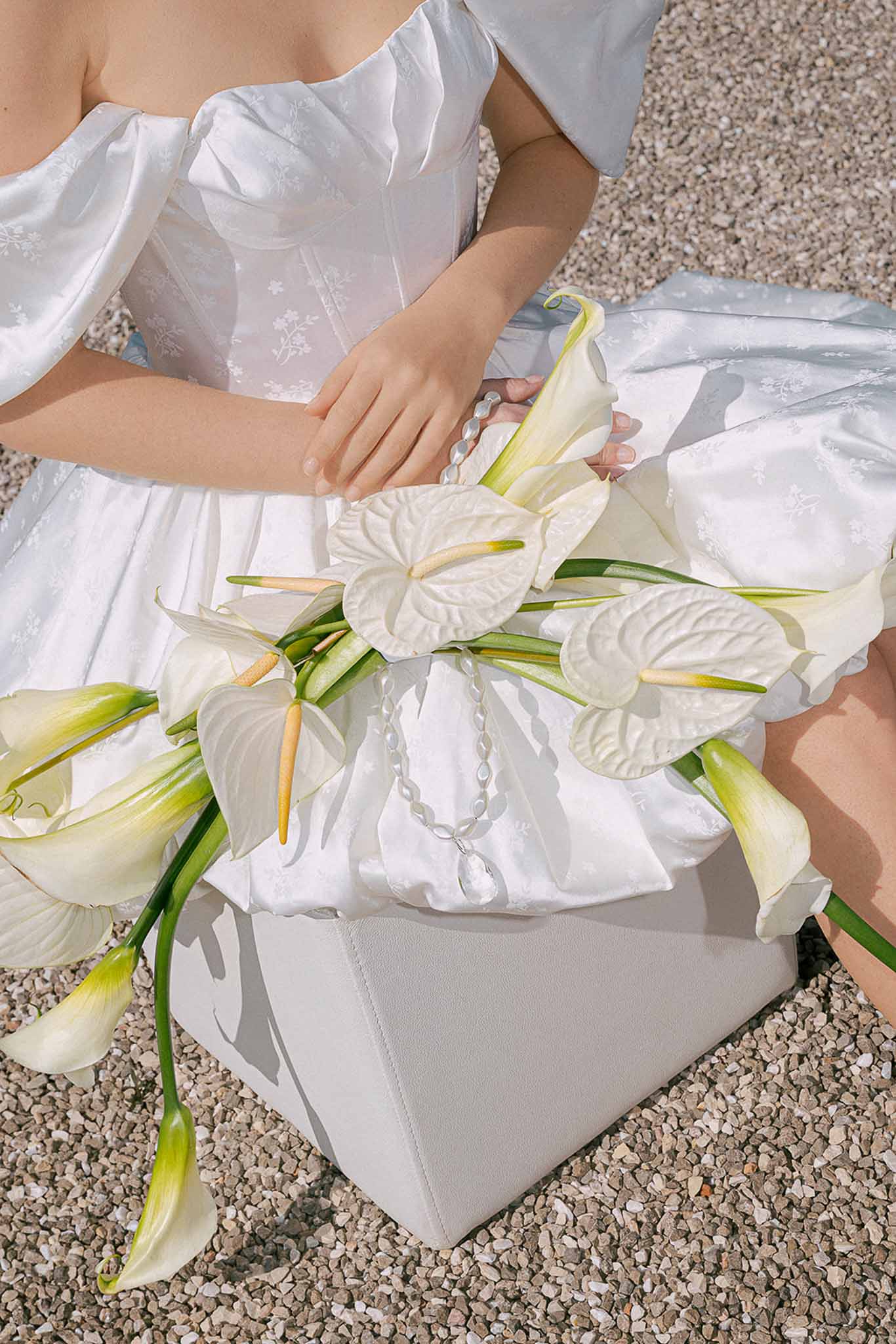 Bride seated outdoors holding white anthurium and calla lily bouquet with crystal chain detail