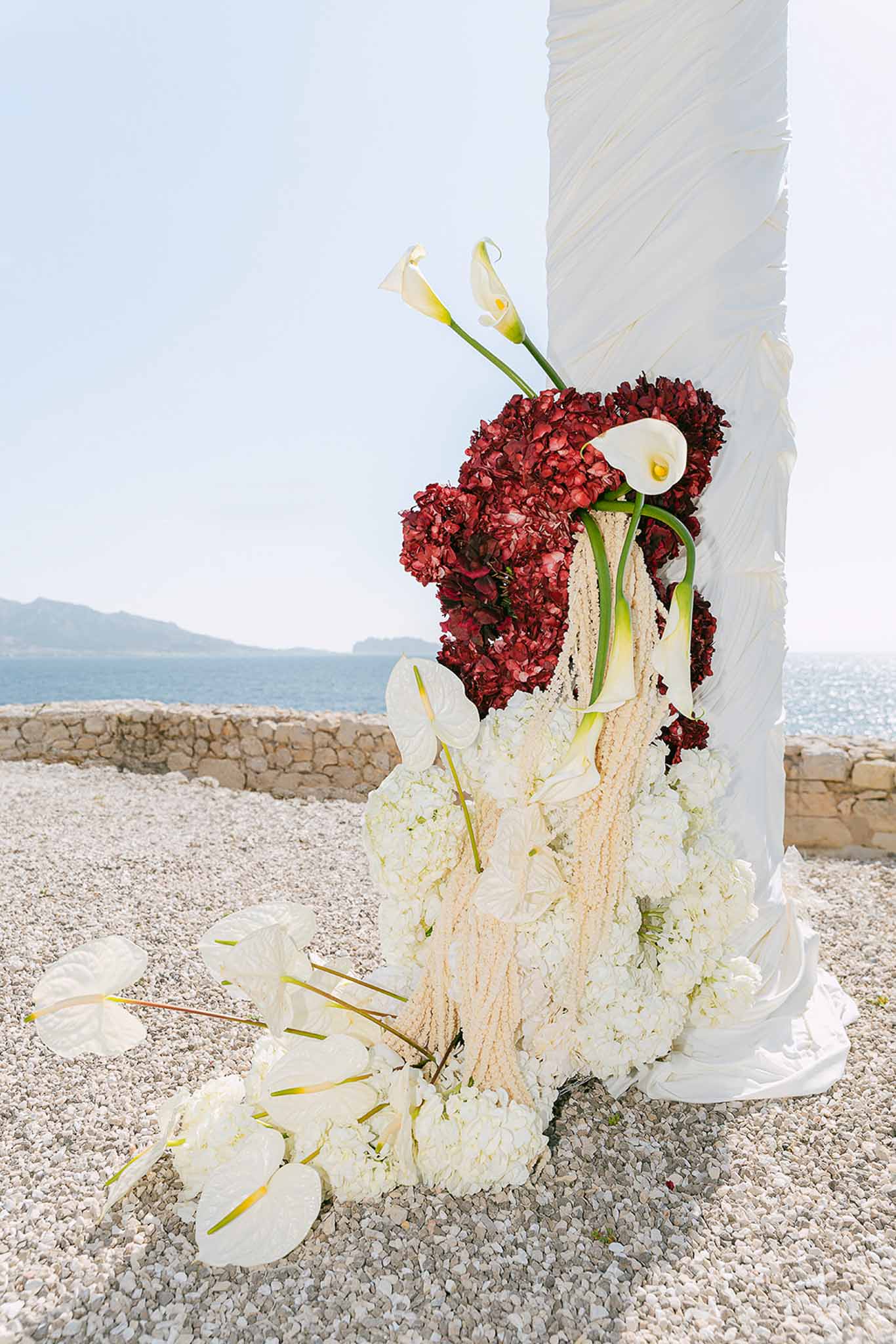 White hydrangea and anthurium column transitioning to burgundy hydrangea with sea view backdrop