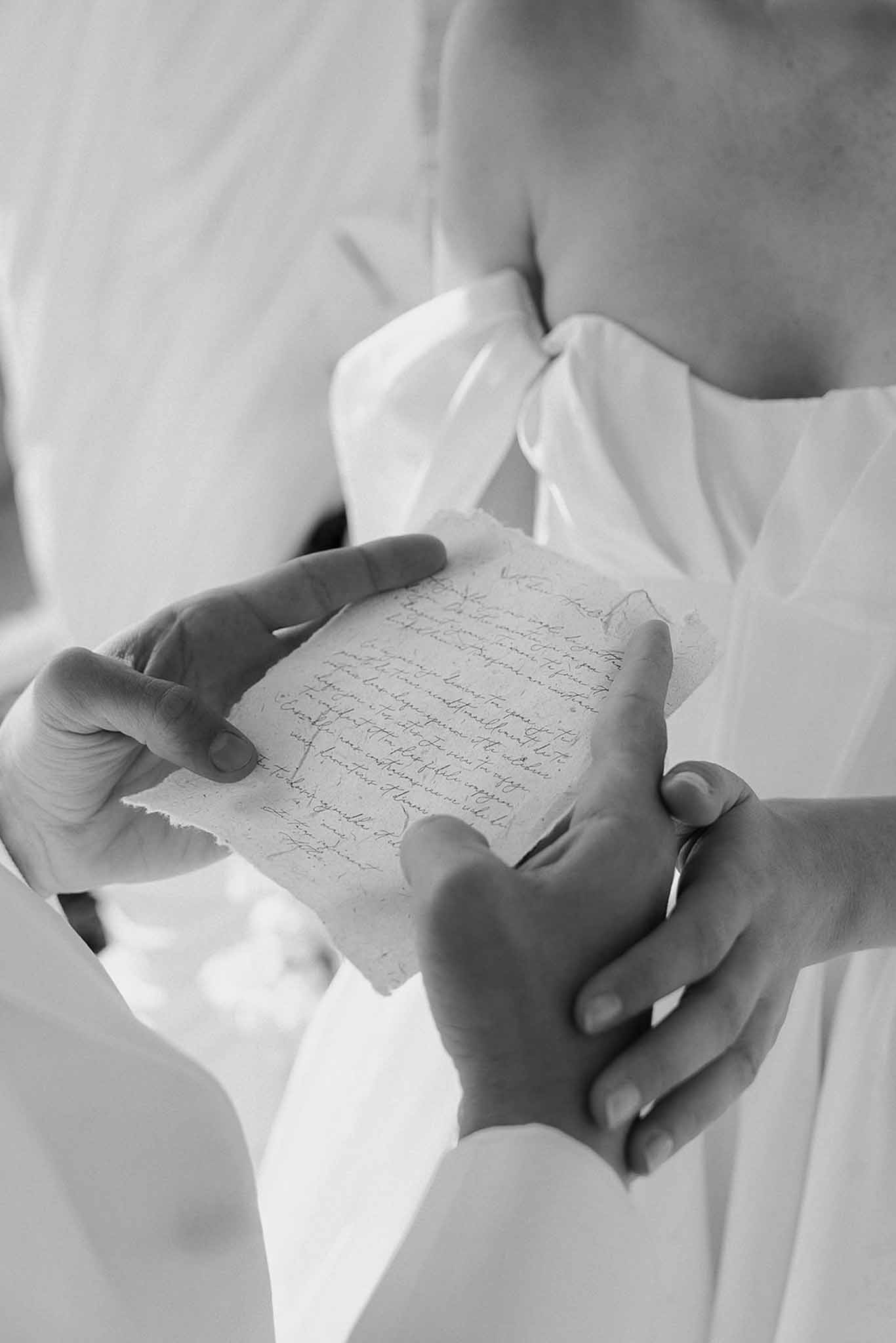 Black and white close-up of hands holding handwritten vow letter on deckle-edge paper