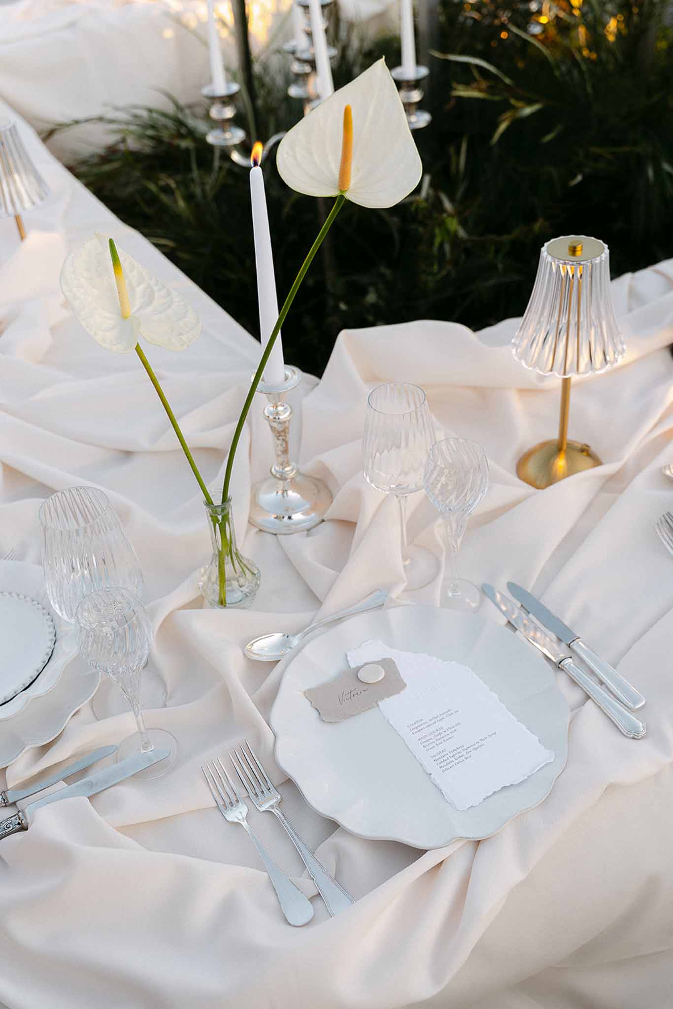 Minimalist reception table with scallop-edged plates, wax seal place cards, white anthurium, and crystal glassware