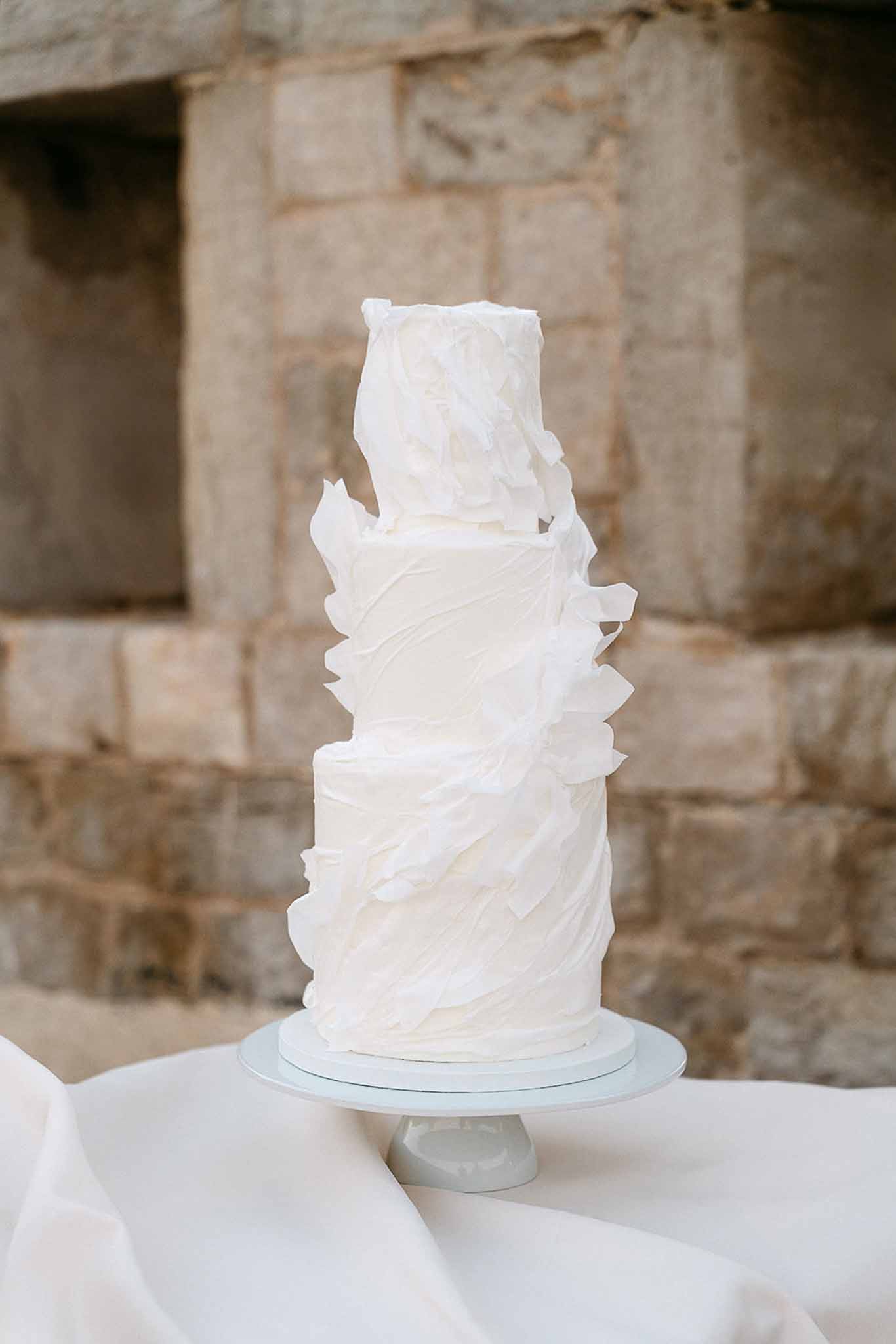 Three-tier ivory buttercream wedding cake with sculptural ruffle petal design on grey ceramic stand