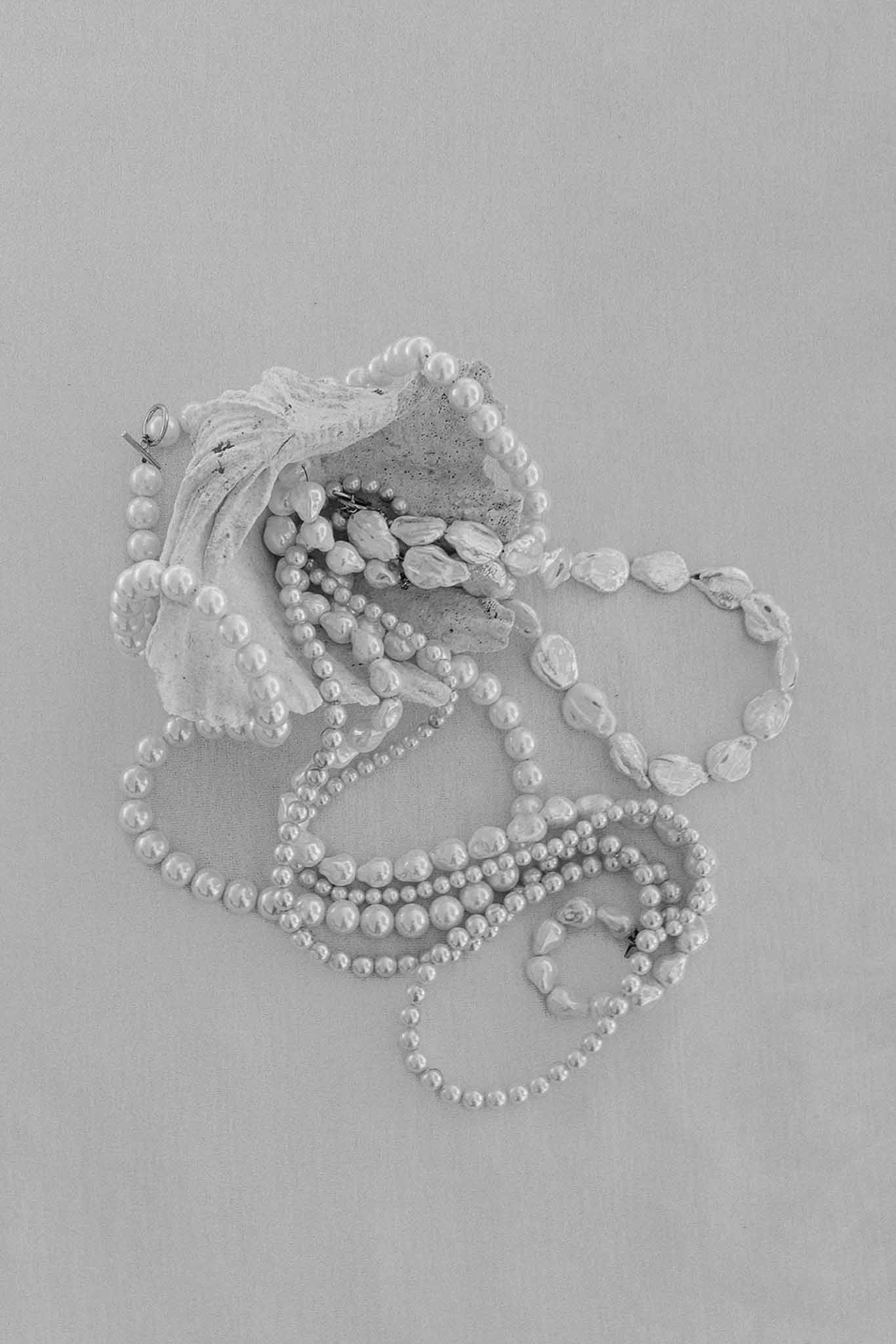Black and white flat lay of bridal pearl necklaces, baroque pearls, and a ring on light fabric