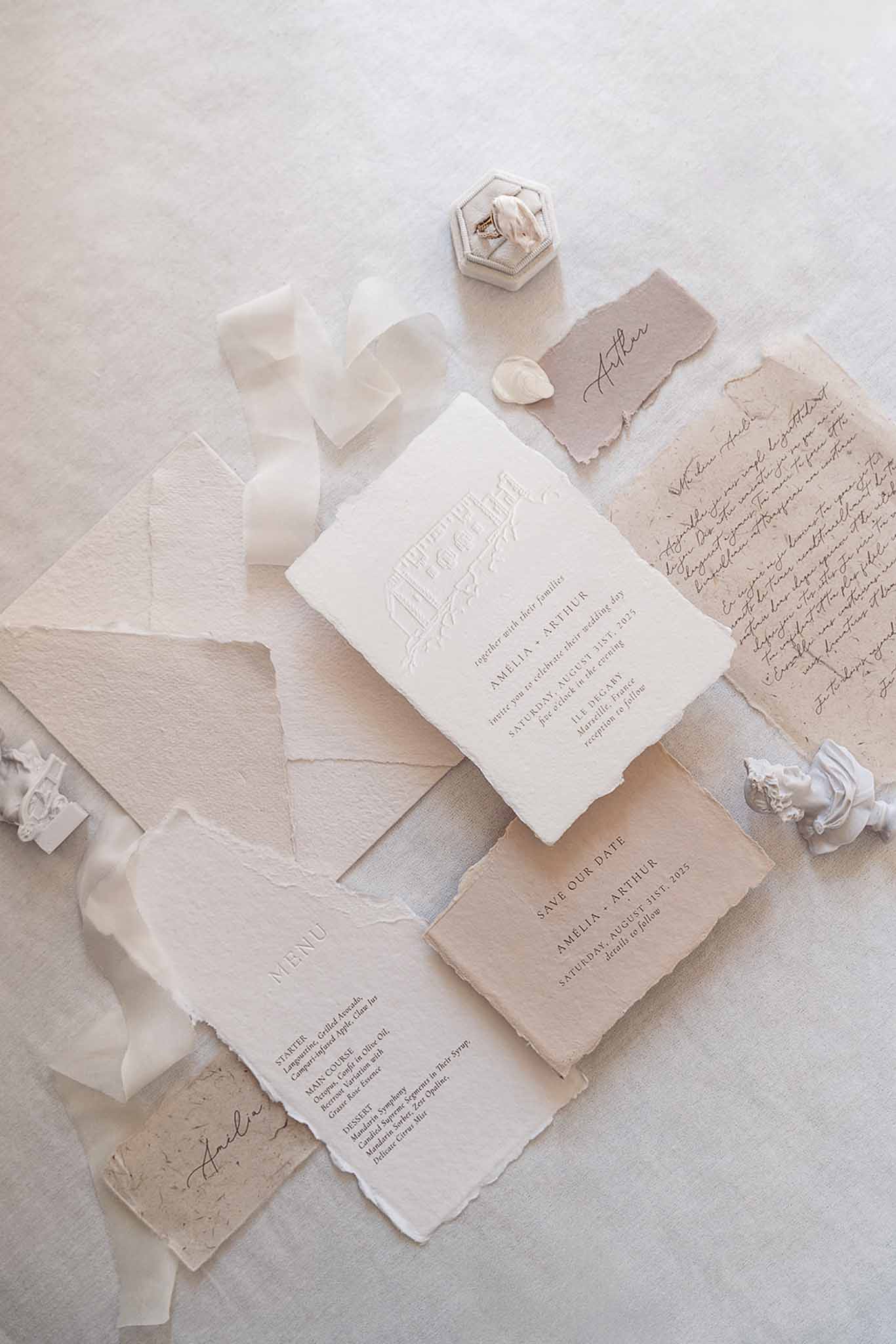 Flat lay of wedding stationery suite with deckle-edge invitation, menu, vow card, ring box, and wax seals