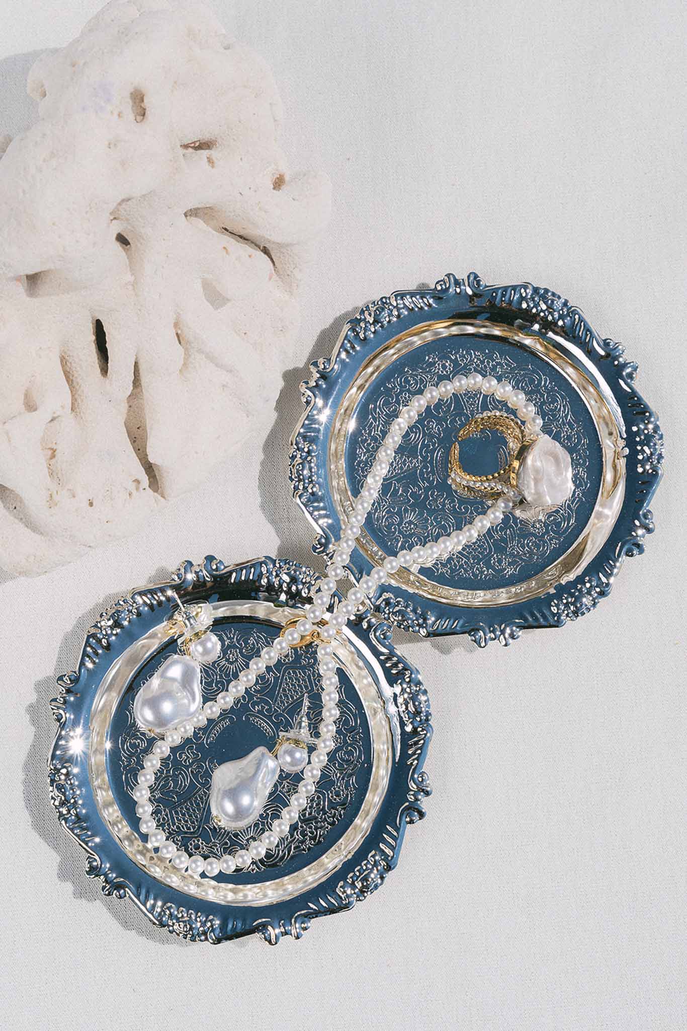 Bridal jewelry flat lay with pearl necklace, baroque pearl earrings, and gold ring on blue embossed trays