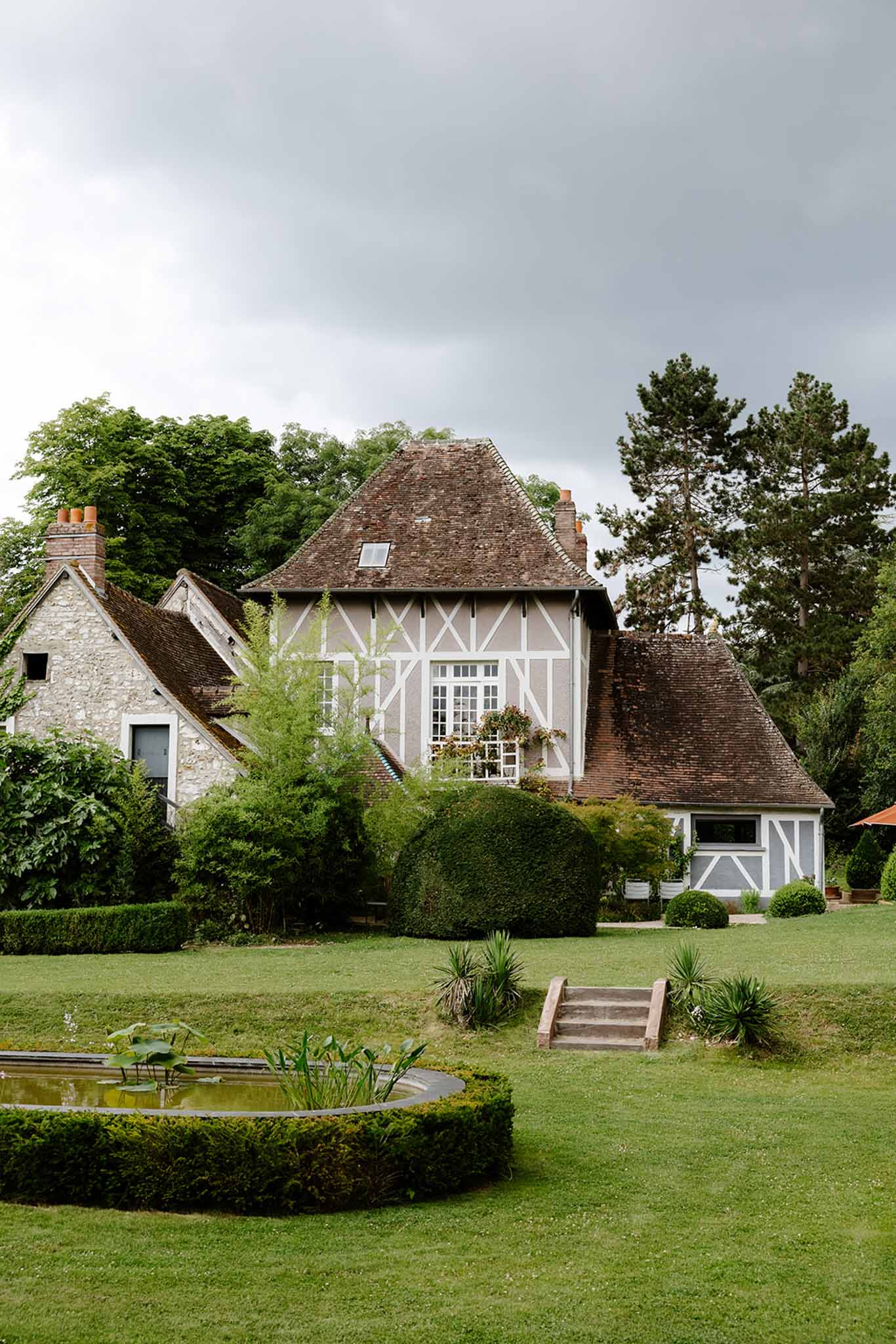 Half-timbered Norman manor house with lily pond clipped hedging and rounded topiary