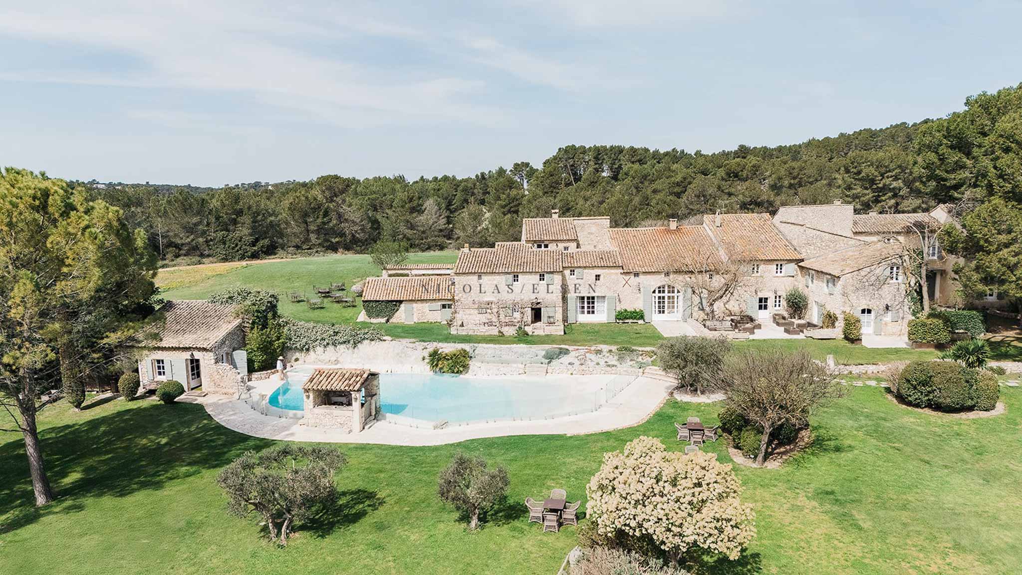 Aerial view of Provencal stone mas complex with freeform pool, olive trees, and garden terraces