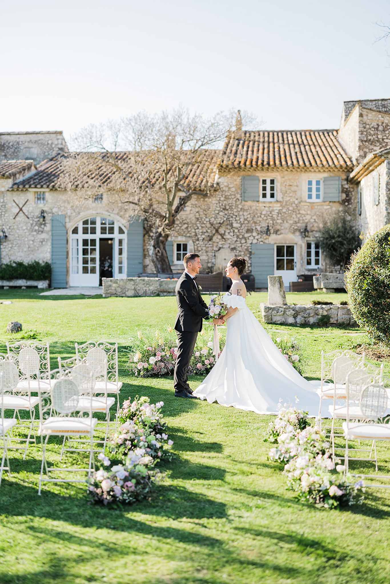 Outdoor ceremony before stone farmhouse with blush and mauve aisle florals and iron garden chairs
