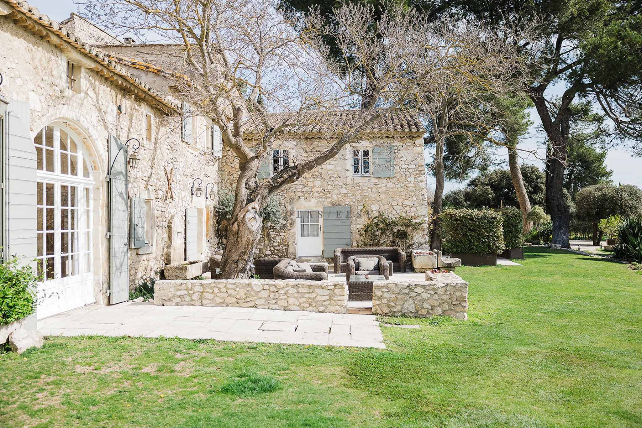 Provencal mas with limestone walls, terracotta roof, sage shutters, and wicker lounge chairs on stone terrace