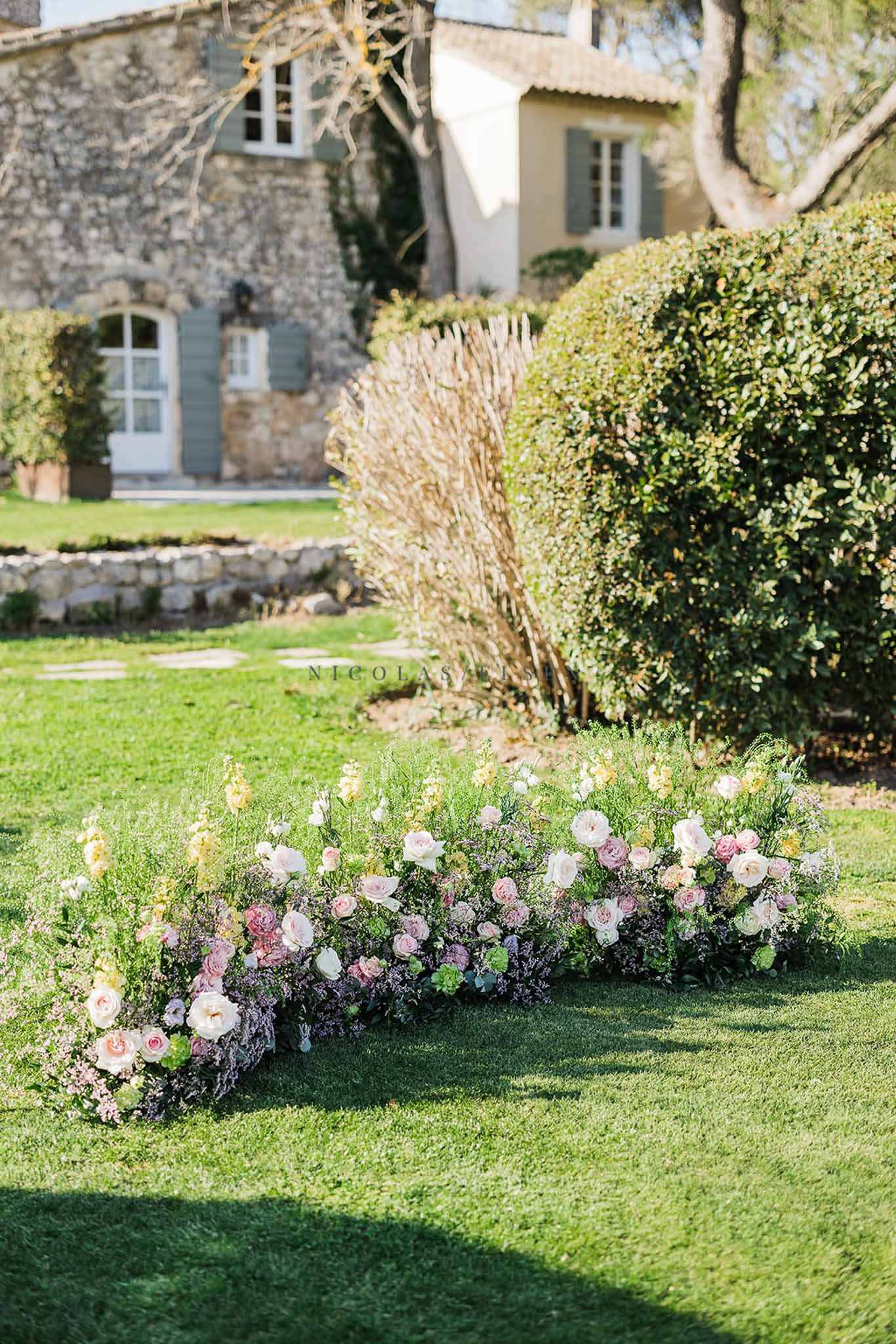 Crescent floral ground installation with mauve roses, blush blooms, and snapdragons on lawn before mas