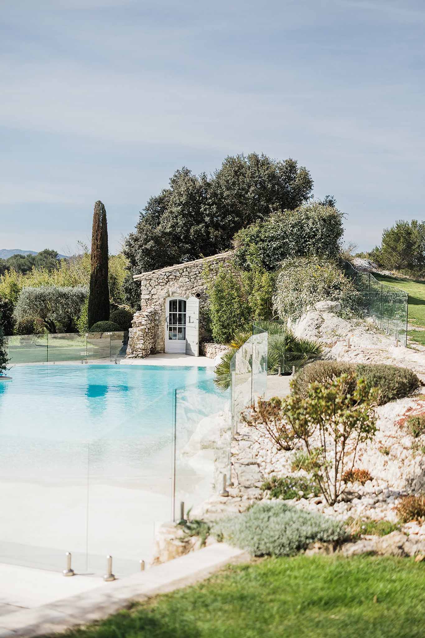 Turquoise swimming pool with glass fence and Provencal stone outbuilding with cypress tree