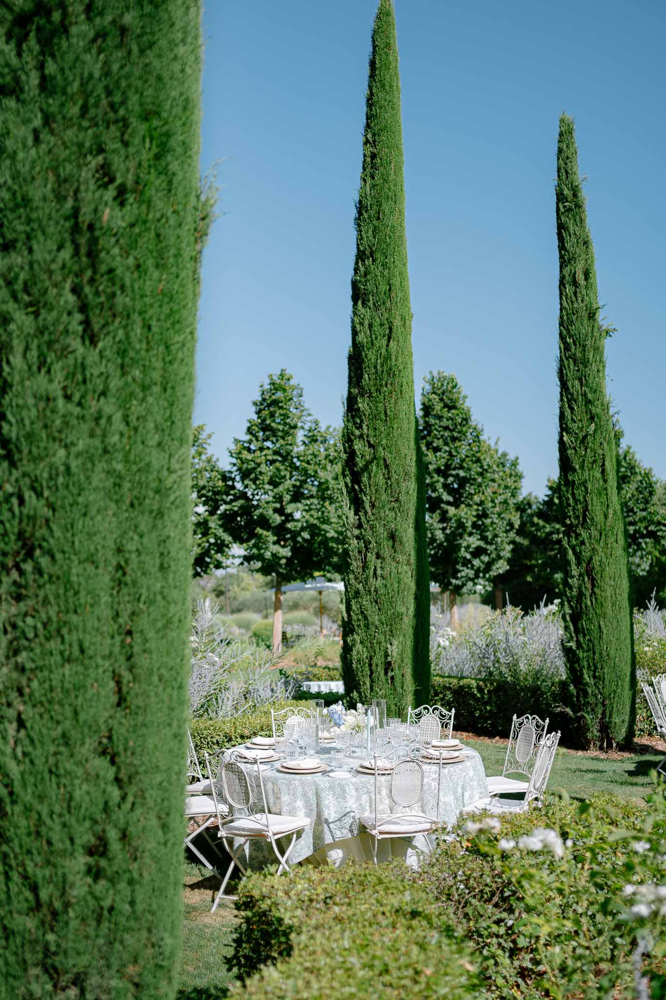 Round reception table with wrought-iron chairs set among Italian cypress trees in formal garden